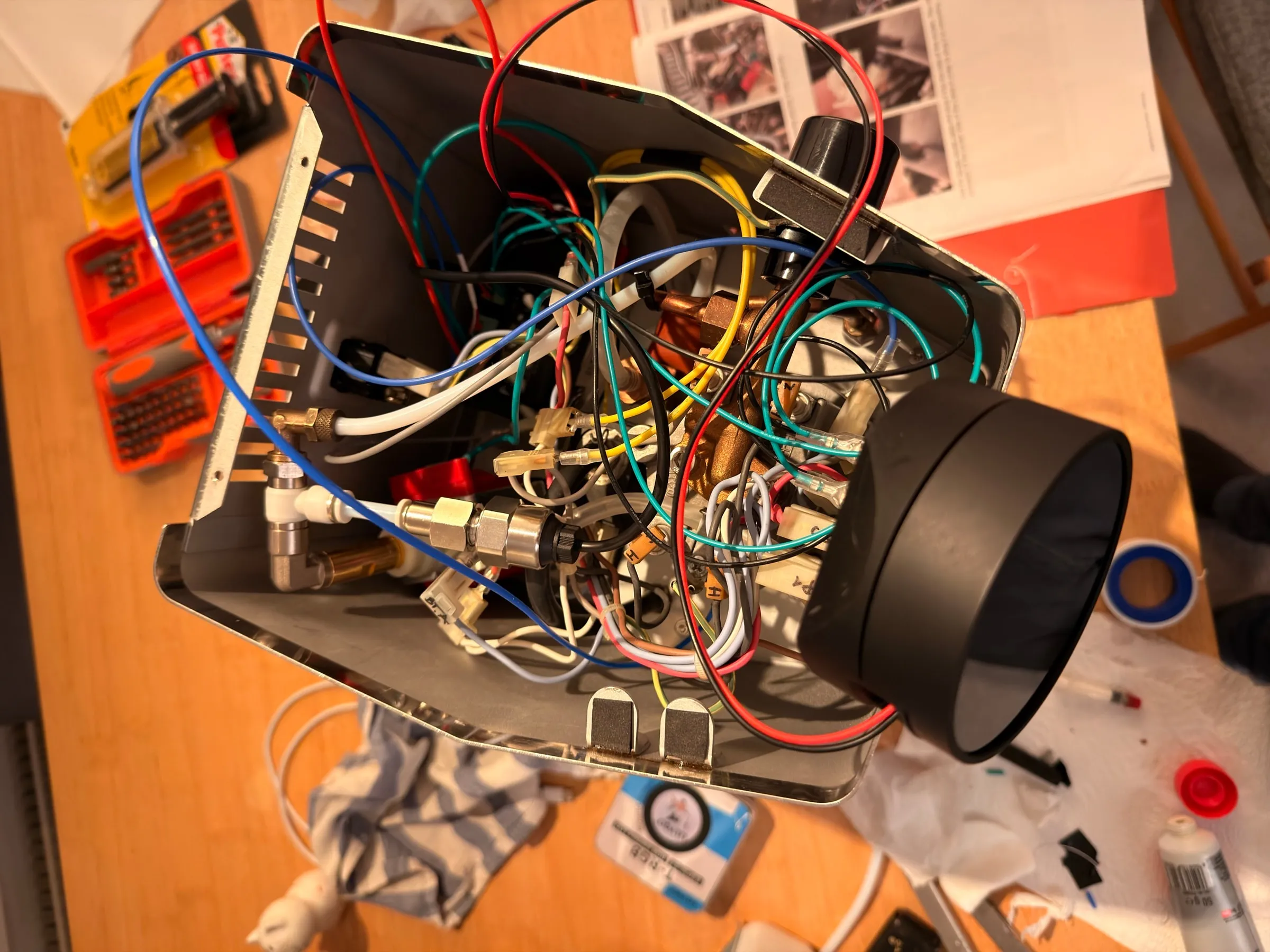 Looking down into the open housing before the first power-up: a dense bundle of red, black, blue, turquoise and yellow wires over the boiler and the brass fittings, the round display lying on the edge of the housing on its cable