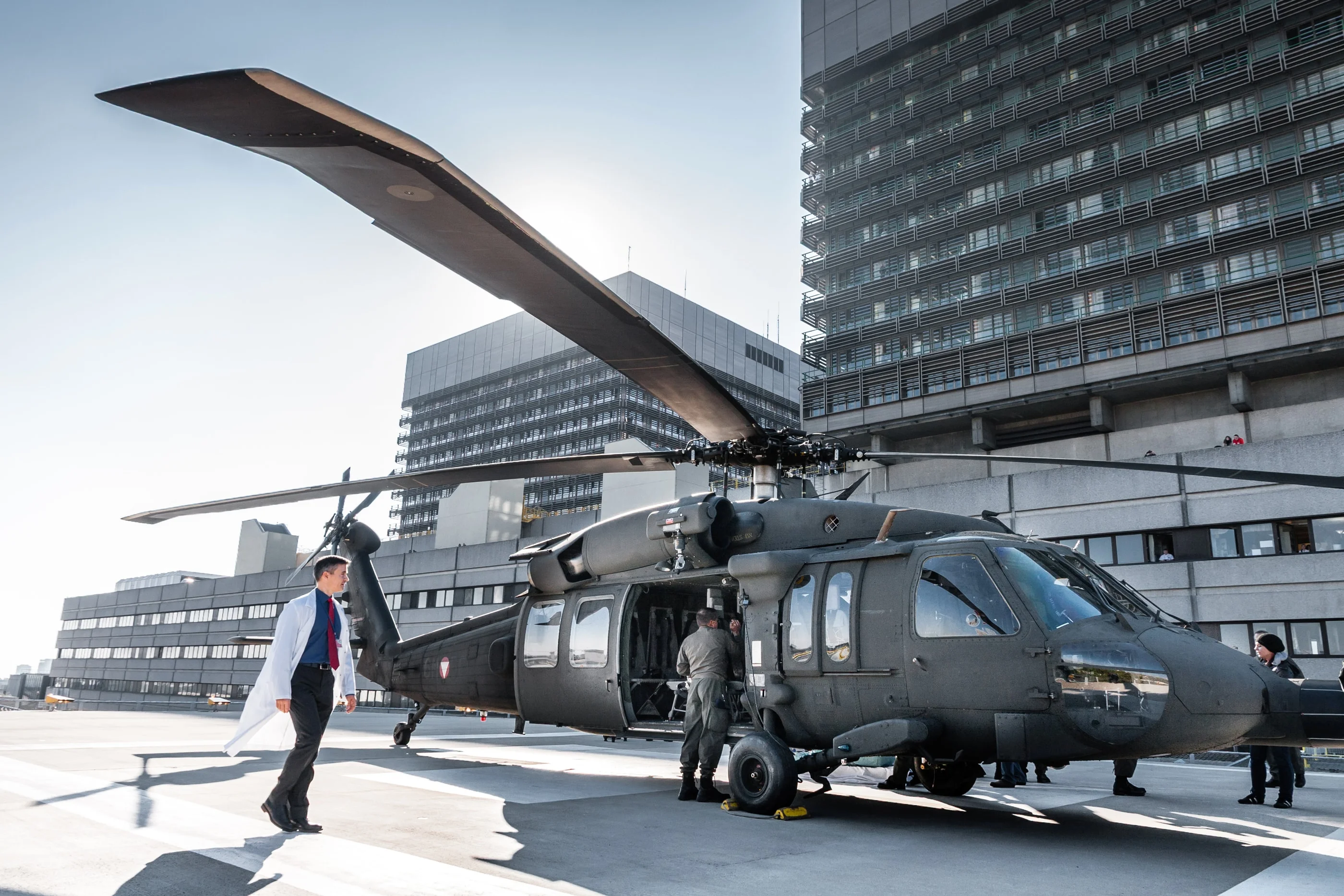 The Black Hawk parked on the rooftop helipad of the AKH hospital, a man in a white coat walking past