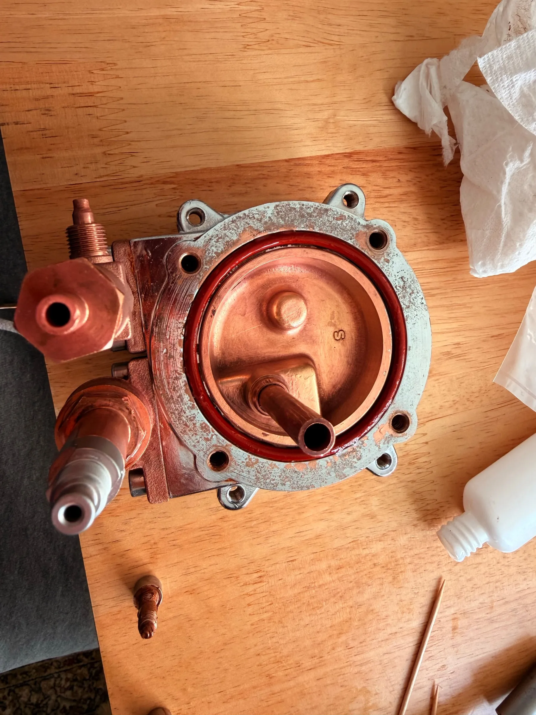 The boiler lying face-up on the table with the large red O-ring freshly seated in its groove around the copper-toned interior, a tube of silicone grease and a cocktail stick beside it