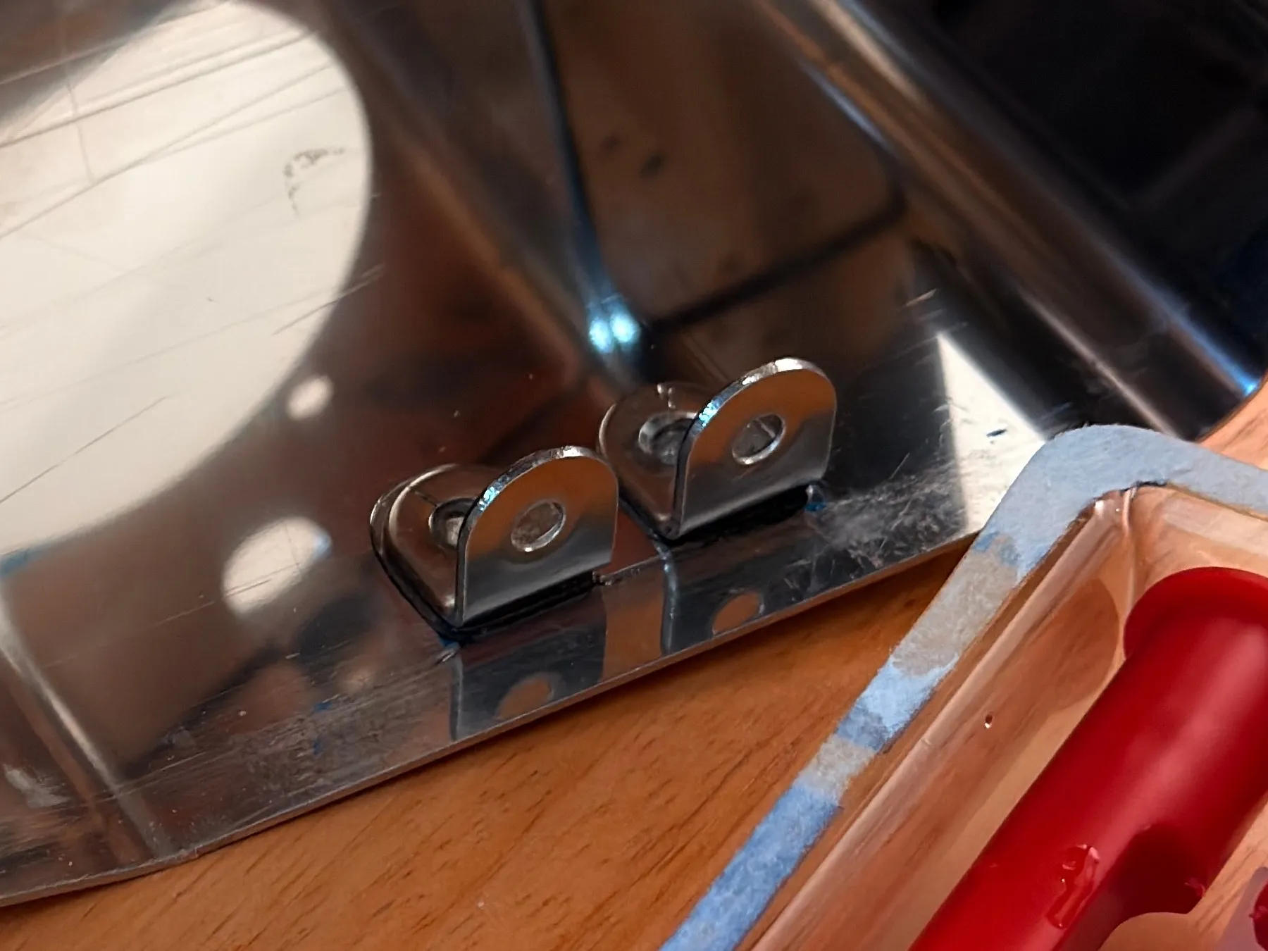 Close-up from the same evening: two small polished steel tabs with a hole each, glued side by side to the inside edge of the housing, the epoxy pack just visible at the right
