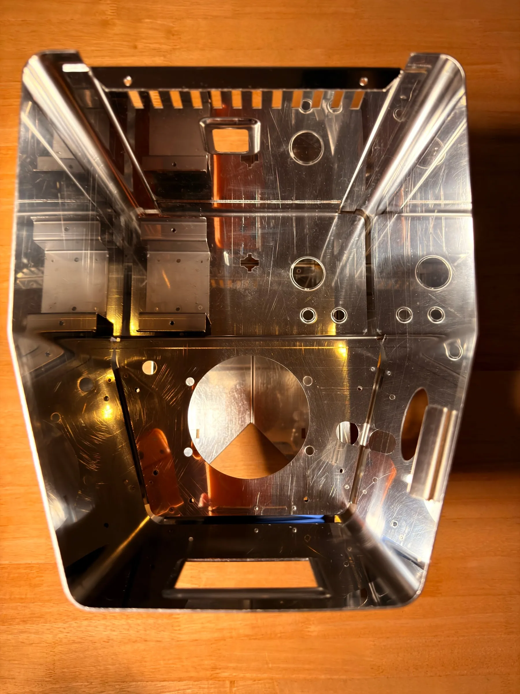 Looking down into the polished stainless housing on a wooden table: every interior surface mirror-bright, the boiler cut-out and the mounting brackets reflecting the room