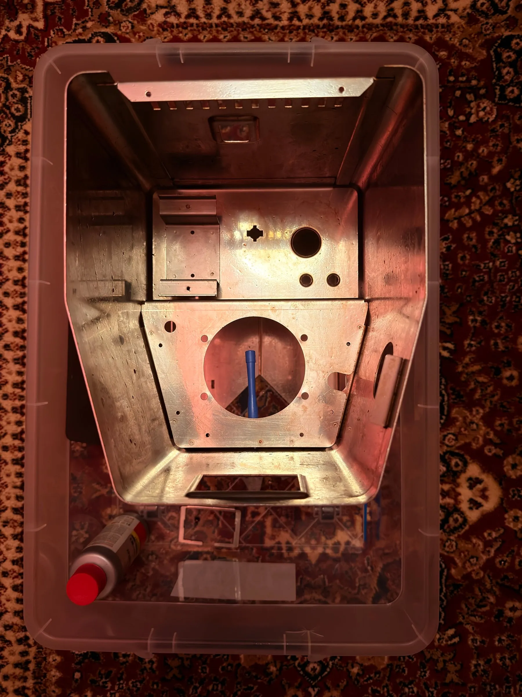 The same base plate one evening later after the rust converter, the orange gone and the steel a calm dark grey, photographed in a plastic storage box under warm light