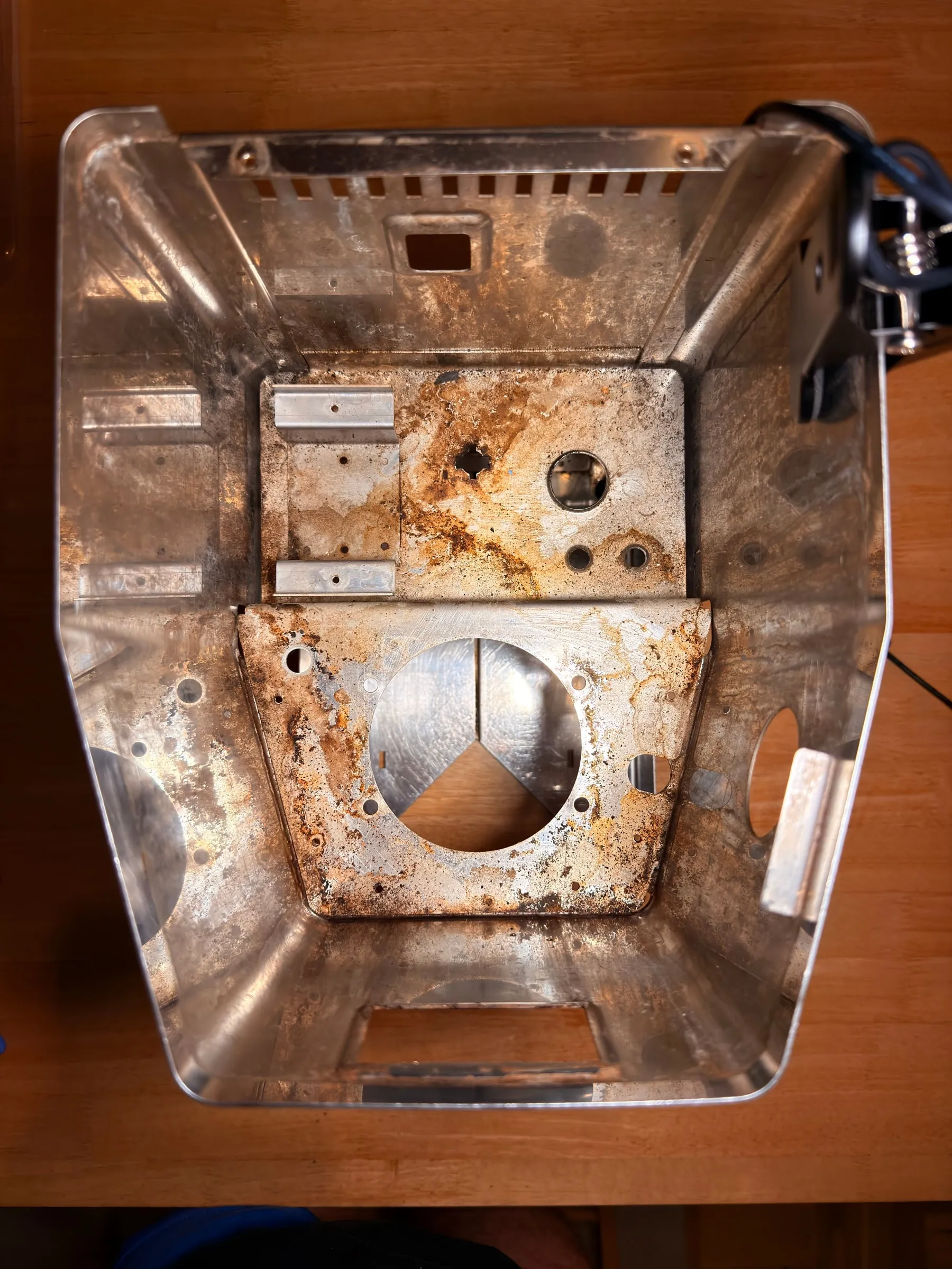 Looking down into the bare stainless housing: the steel base plate and the pump mount are covered in orange-brown flash rust around the round boiler cut-out