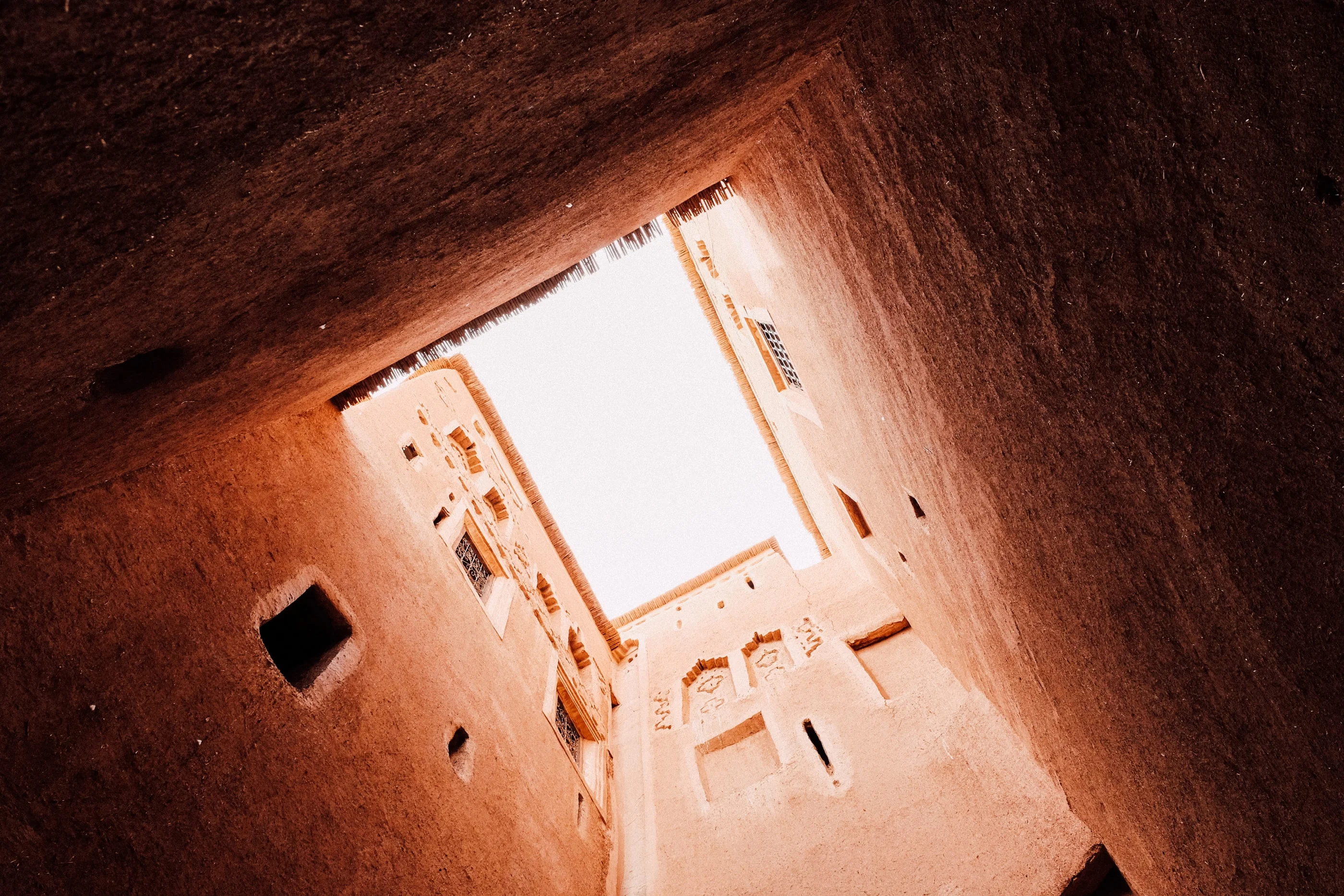 View straight up through the courtyard of a mud-brick kasbah towards the bright sky
