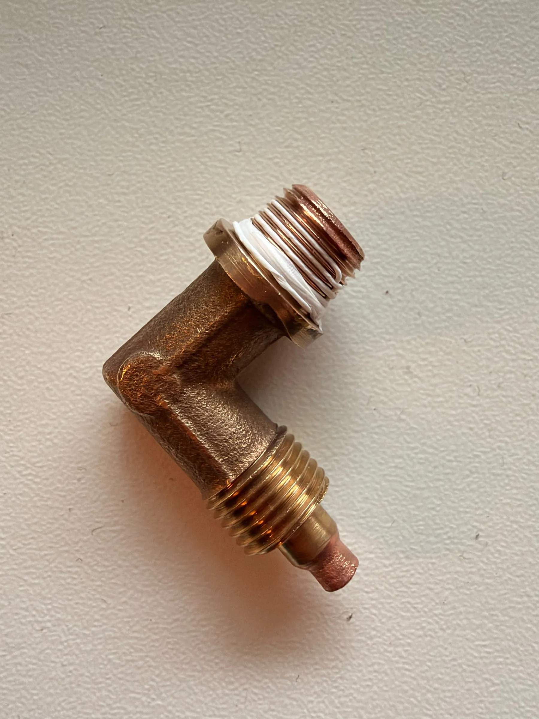 The brass elbow fitting on a white surface with PTFE tape neatly wound on the thread, the first turns left bare
