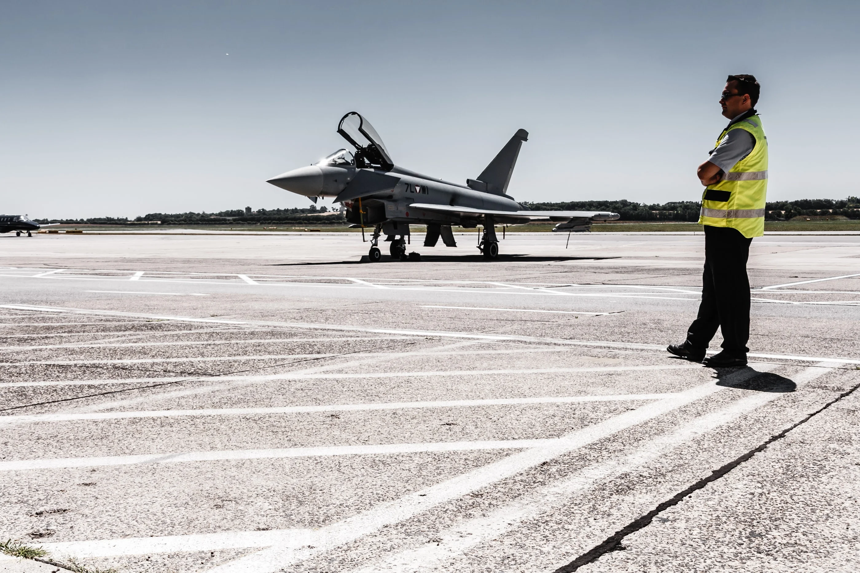 Airport worker in a high-visibility vest on the apron, a Eurofighter in the background