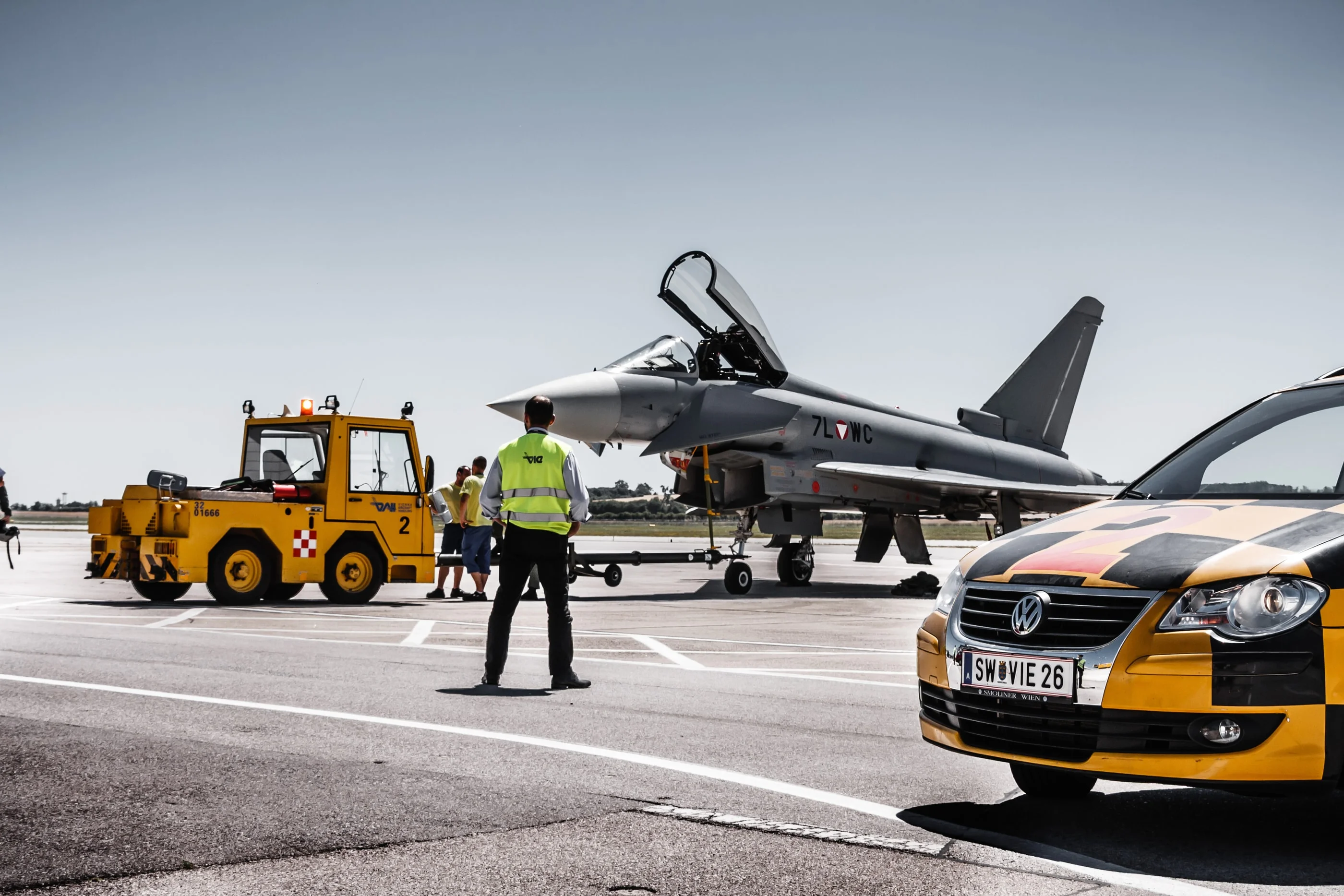 Follow-me car and tow tractor in front of a Eurofighter, a marshaller standing between them