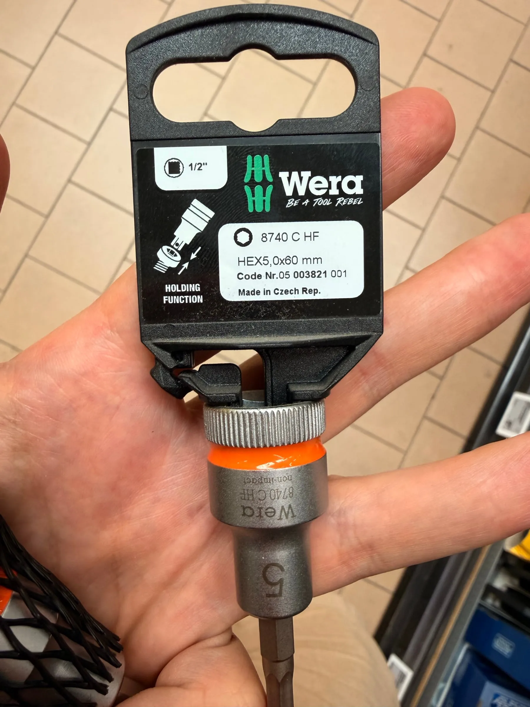 A hand holding a Wera 5 mm hex socket with half-inch drive, still on its packaging card, in an aisle of the hardware store