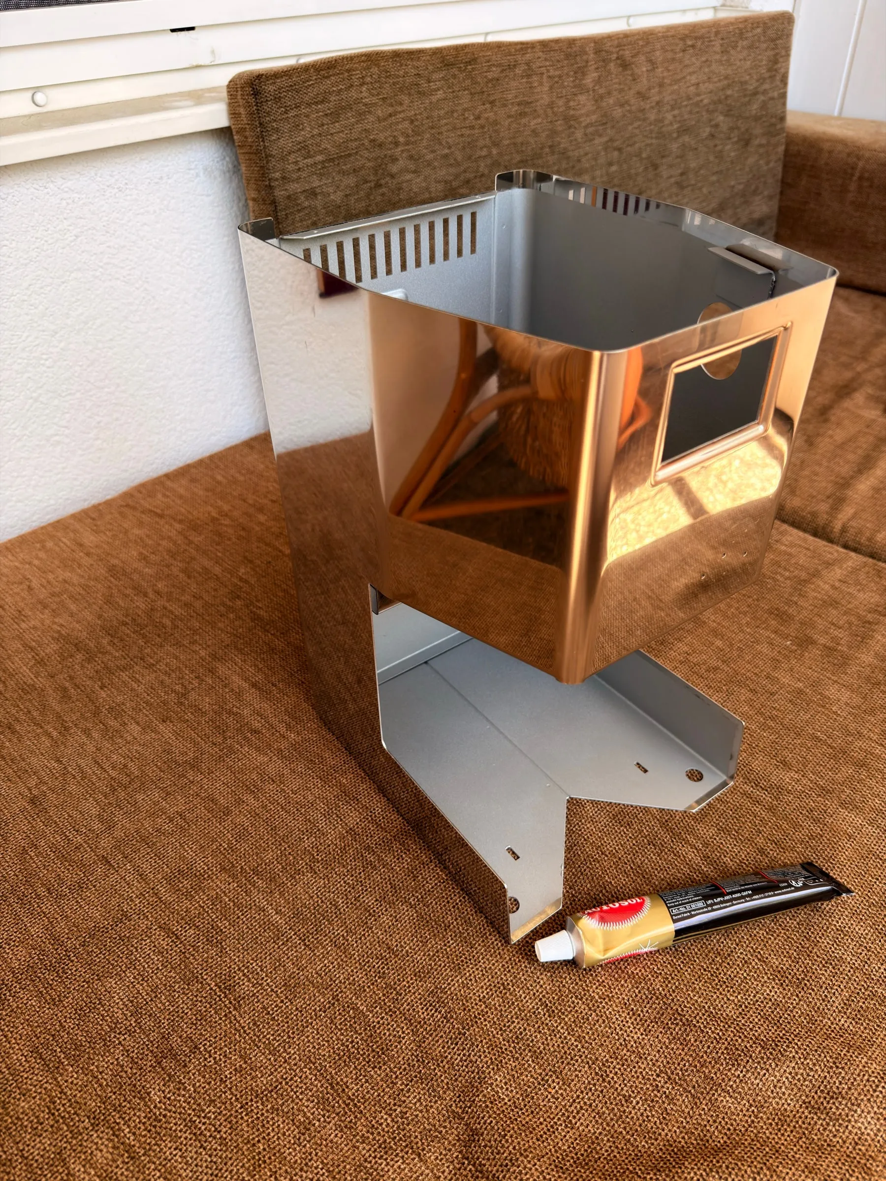 The finished housing standing on a brown blanket: the stainless outside polished to a mirror that reflects a wicker chair, the inside matt aluminium silver, a tube of Autosol metal polish lying in front