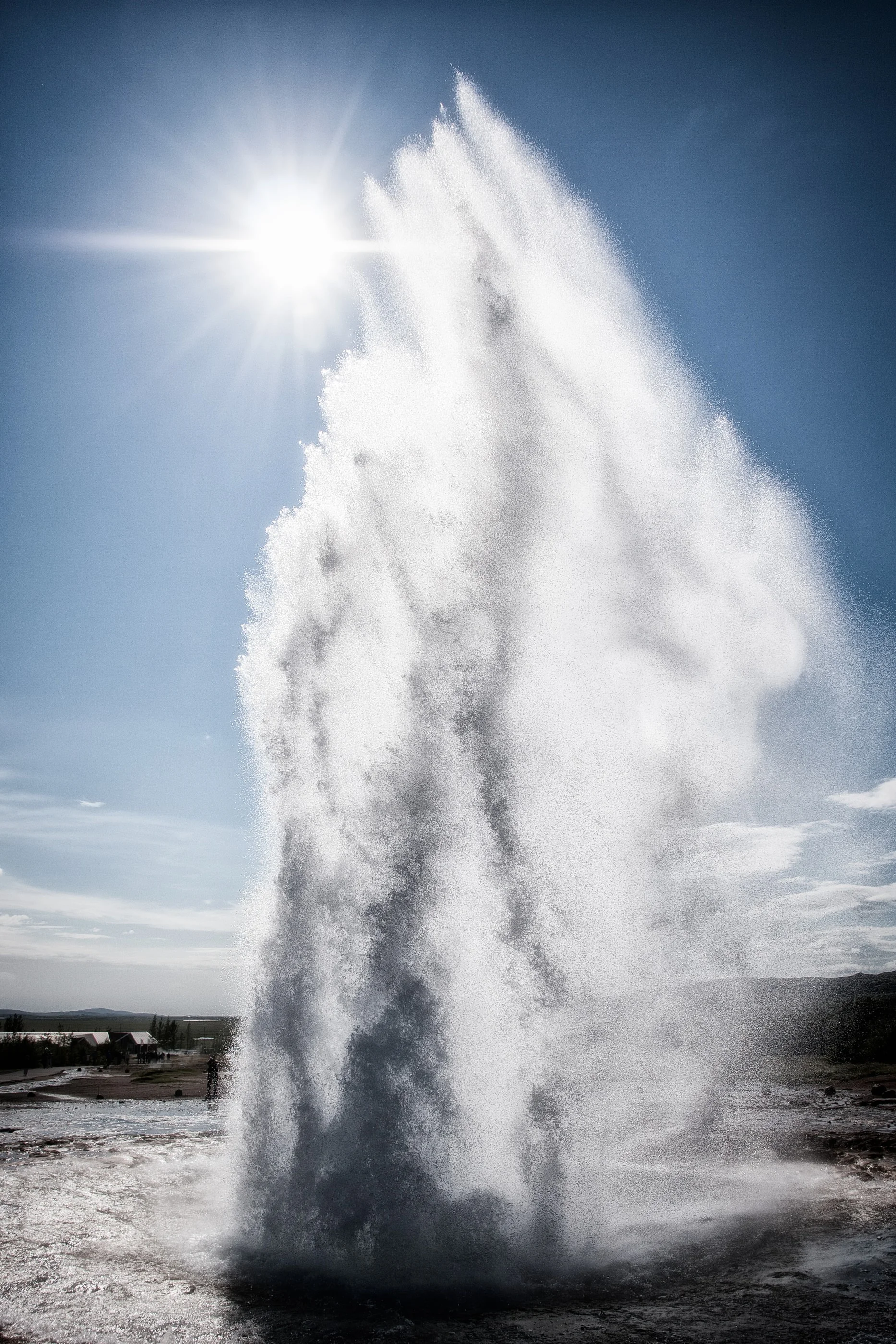 Geyser erupting in a tall column of water and steam against the sun