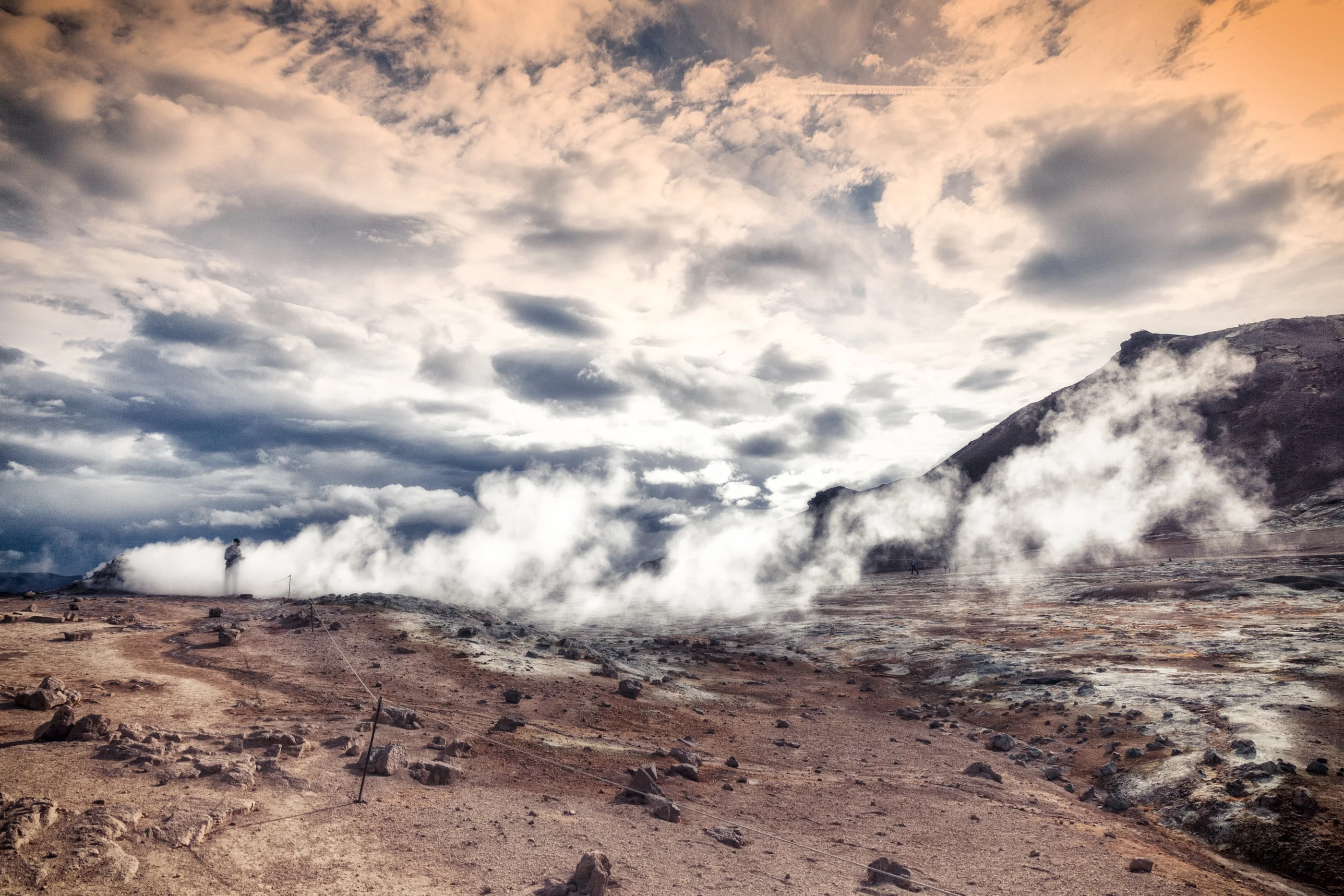 Steam rising from a geothermal field under dramatic clouds