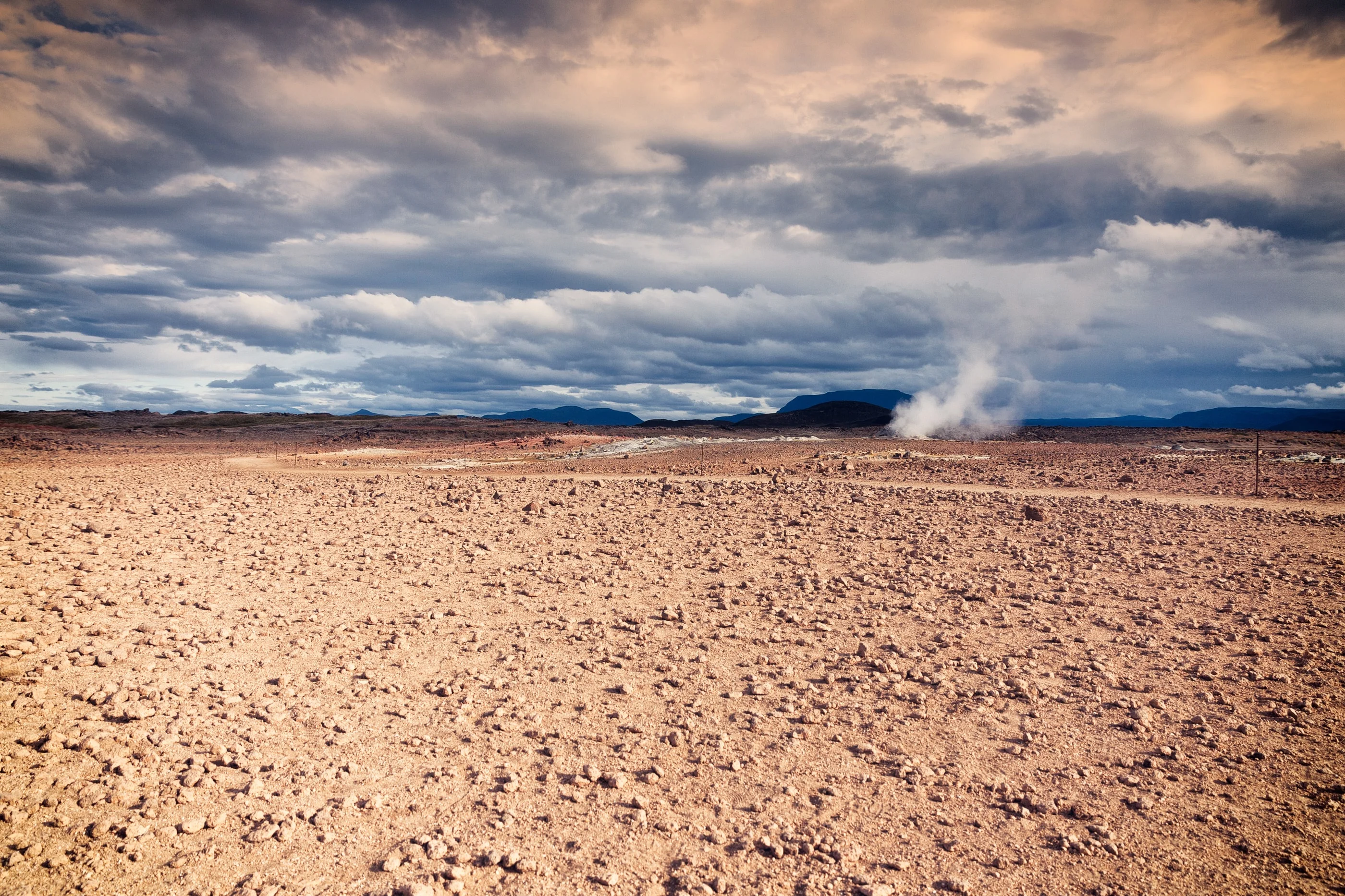 Flat brown plain with a plume of steam in the distance under heavy clouds