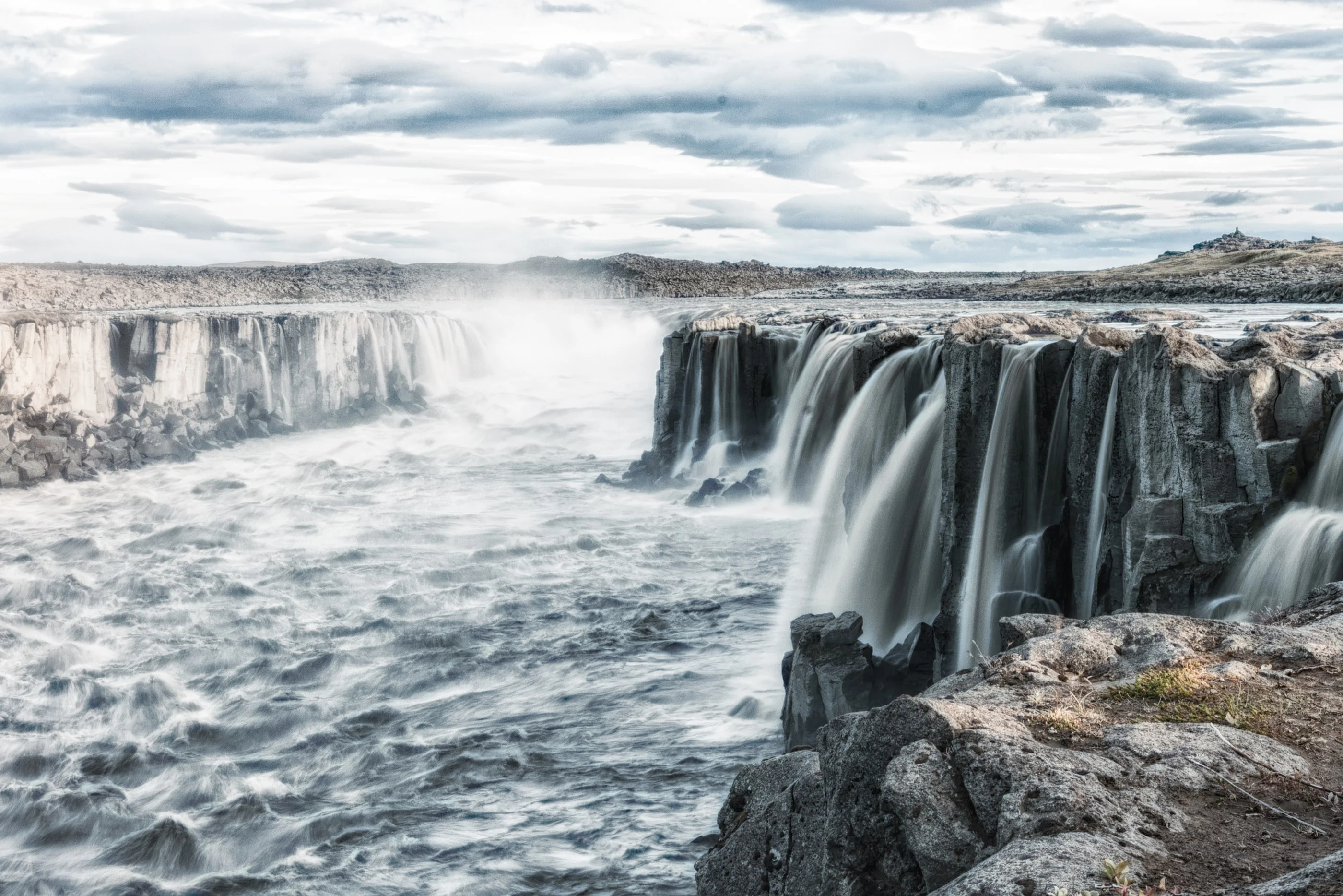 Wide waterfall pouring over a basalt cliff into a gorge