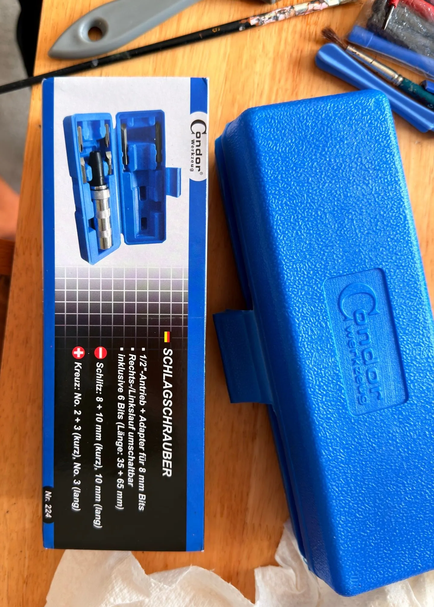 The manual impact driver in its box next to the blue plastic case, the label listing a half-inch drive, switchable direction and six bits for slotted and Phillips screws