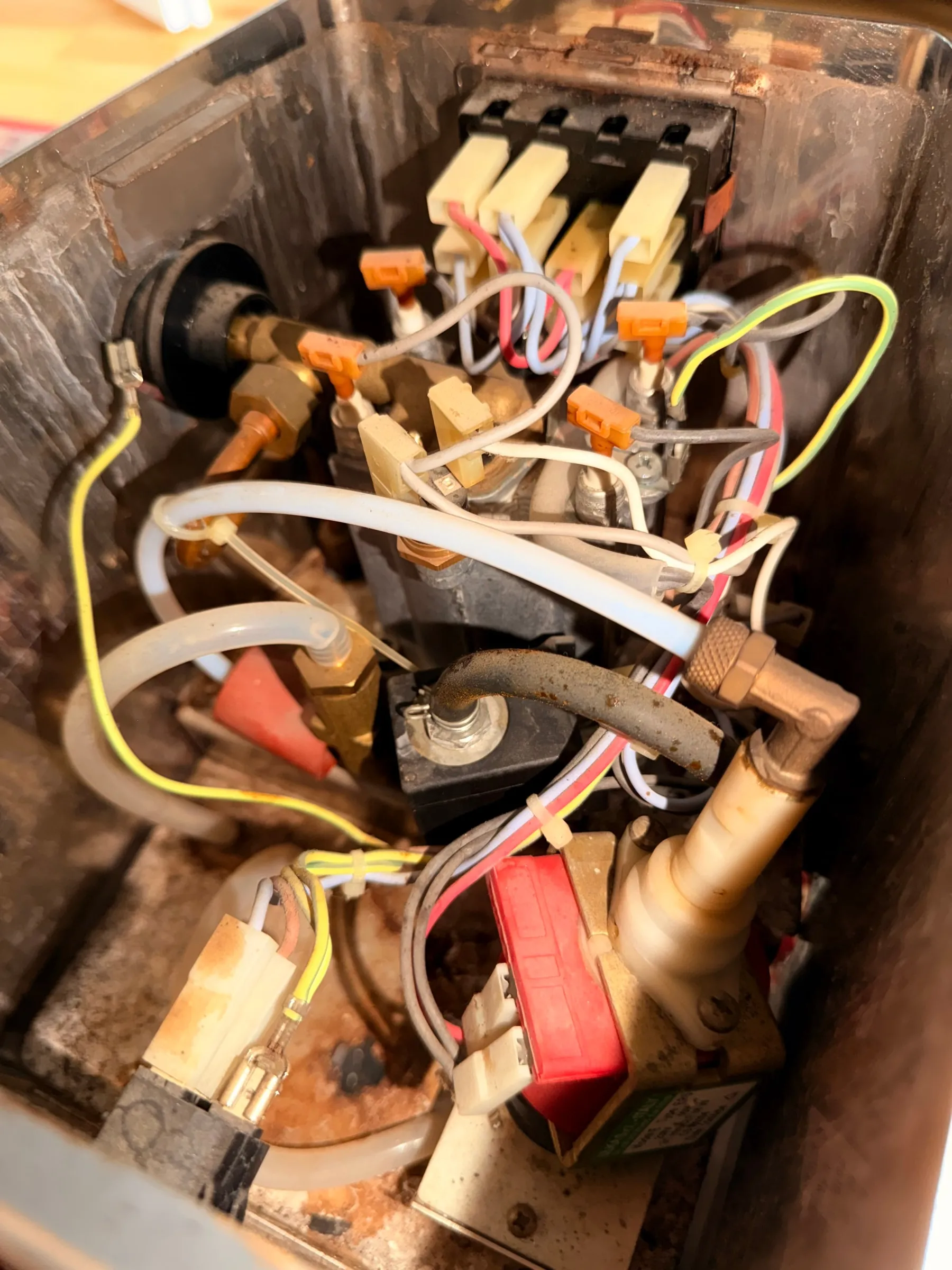 Looking down into the open housing: the original wiring loom with ivory spade connectors, the brass steam valve, the aluminium boiler, the red Ulka pump and rust stains on the base plate