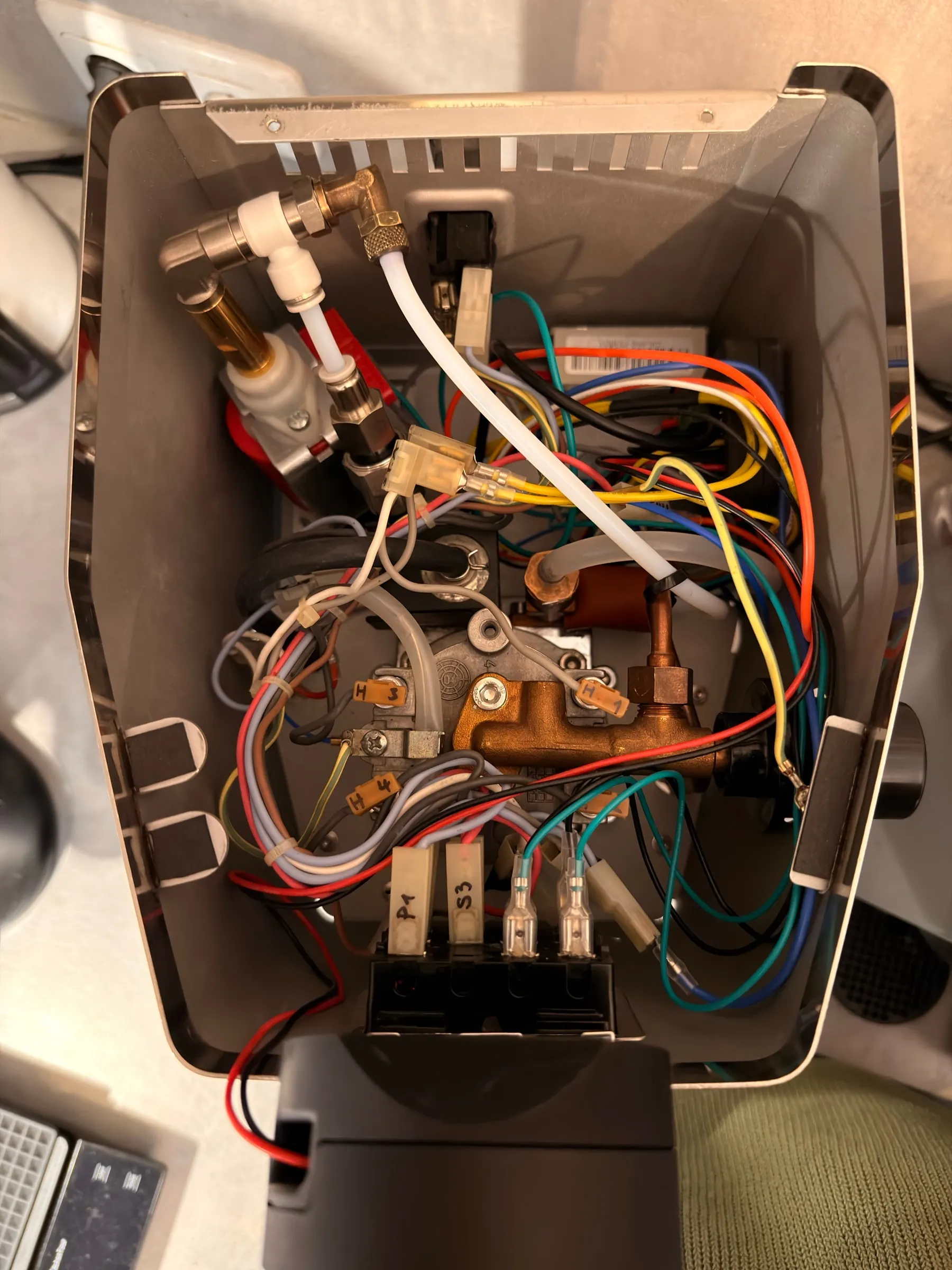 Looking down into the open housing right after the self-test: the boiler with its brass fittings, the white T-piece and hoses, the labelled connectors and the coloured wires, every joint dry