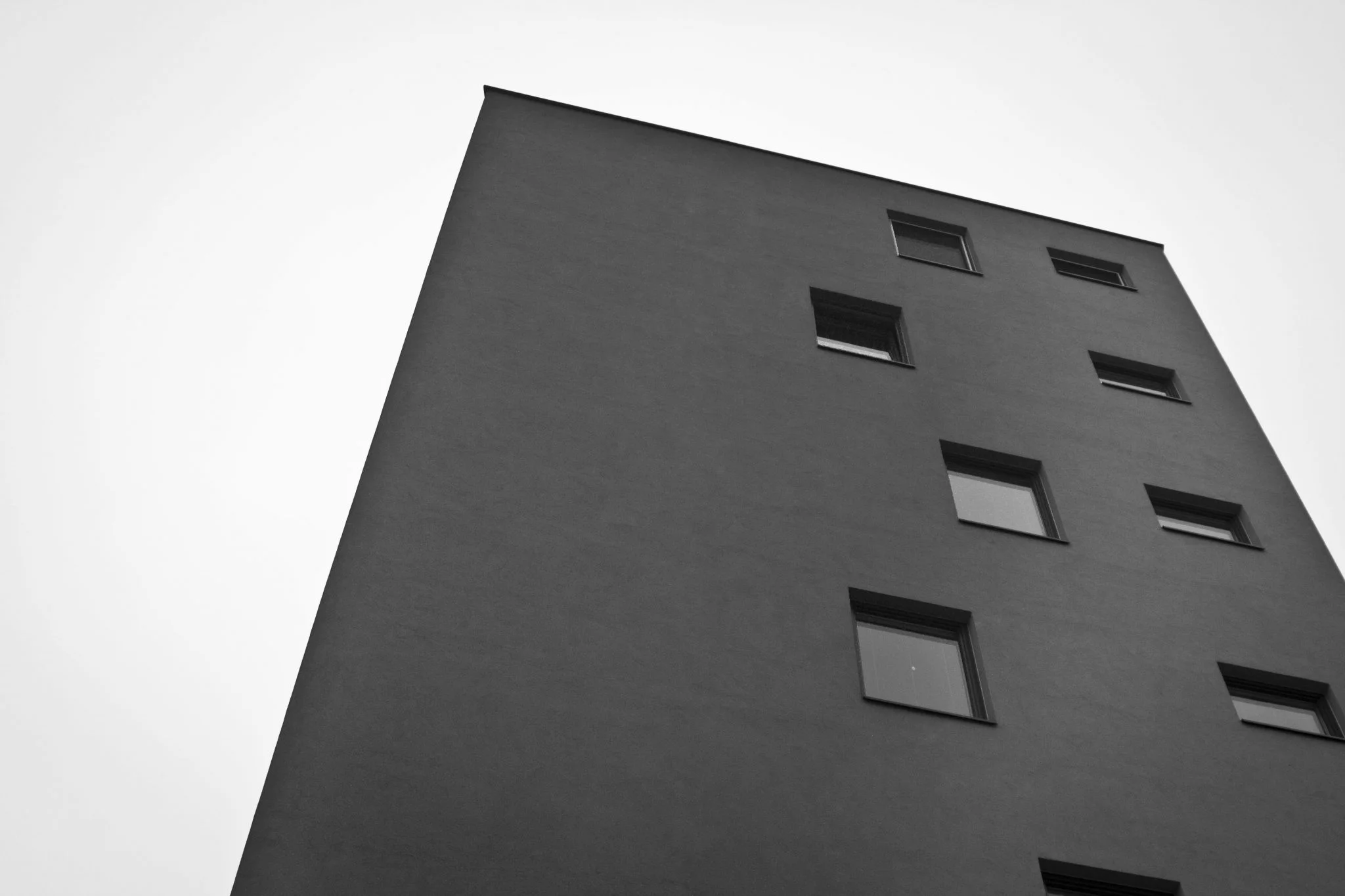 Plain dark facade with small windows tilting against a white sky
