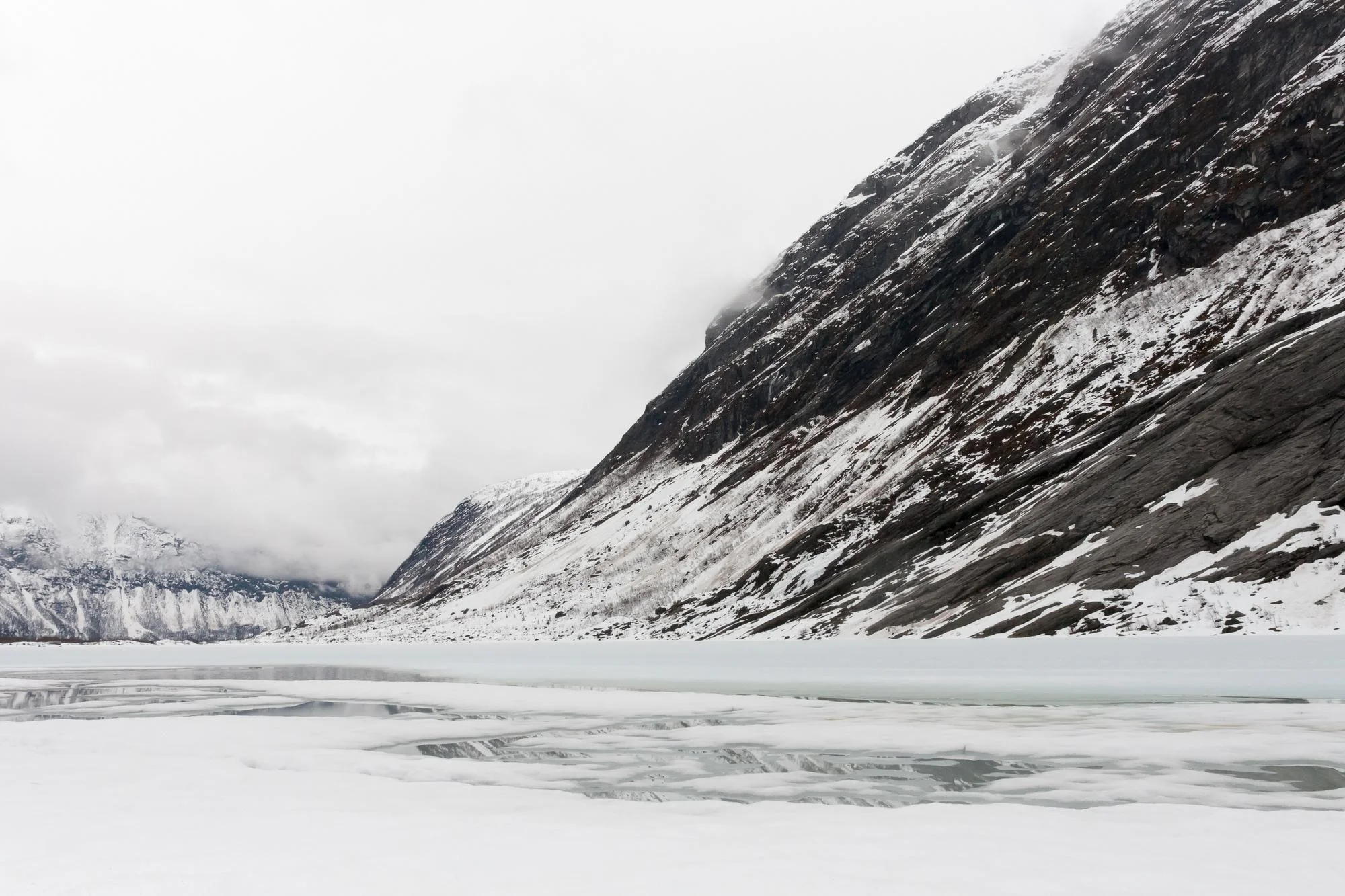 Frozen lake below a steep snowy mountainside