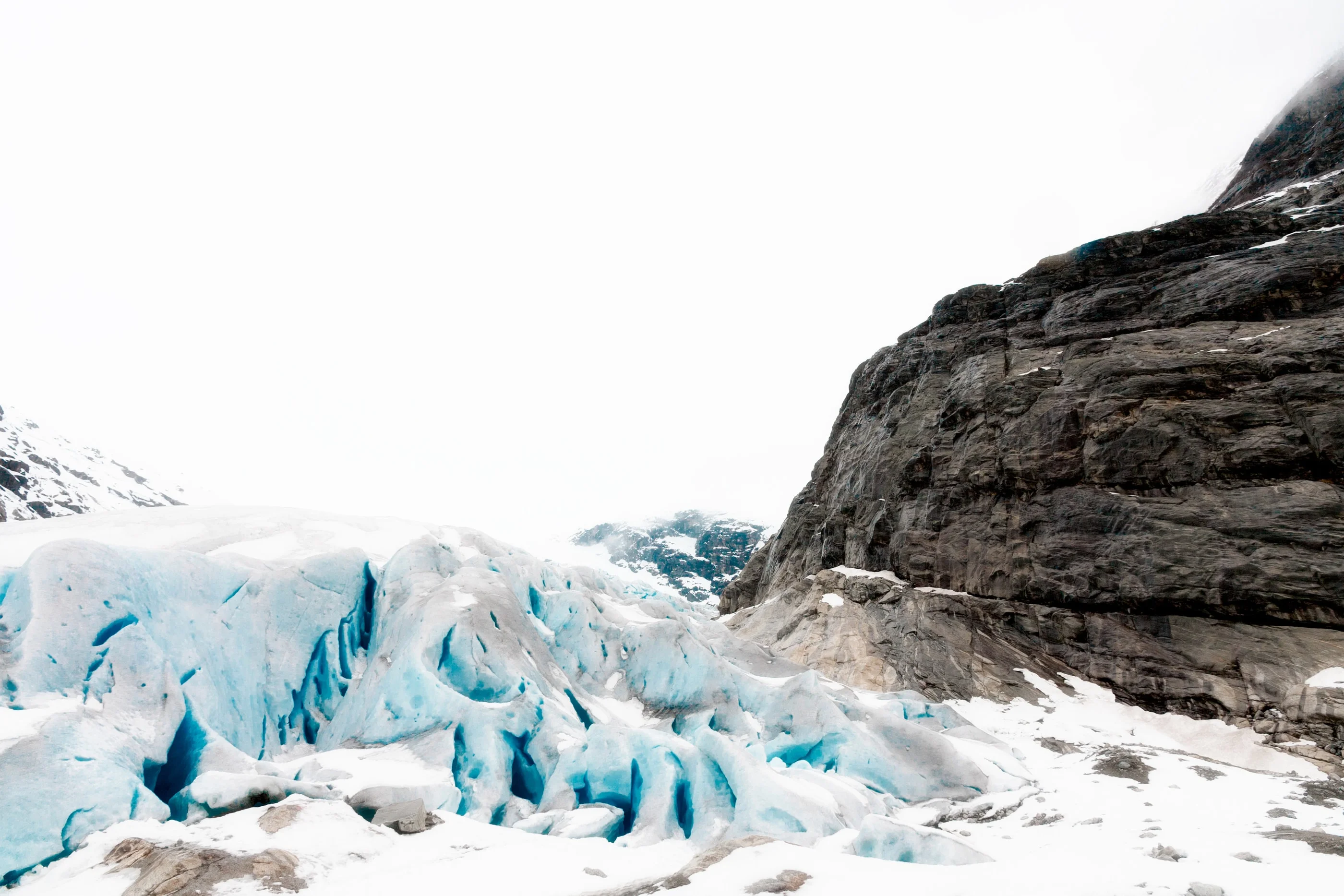 Tongue of the blue Nigard Glacier between snowy slopes and a dark rock face