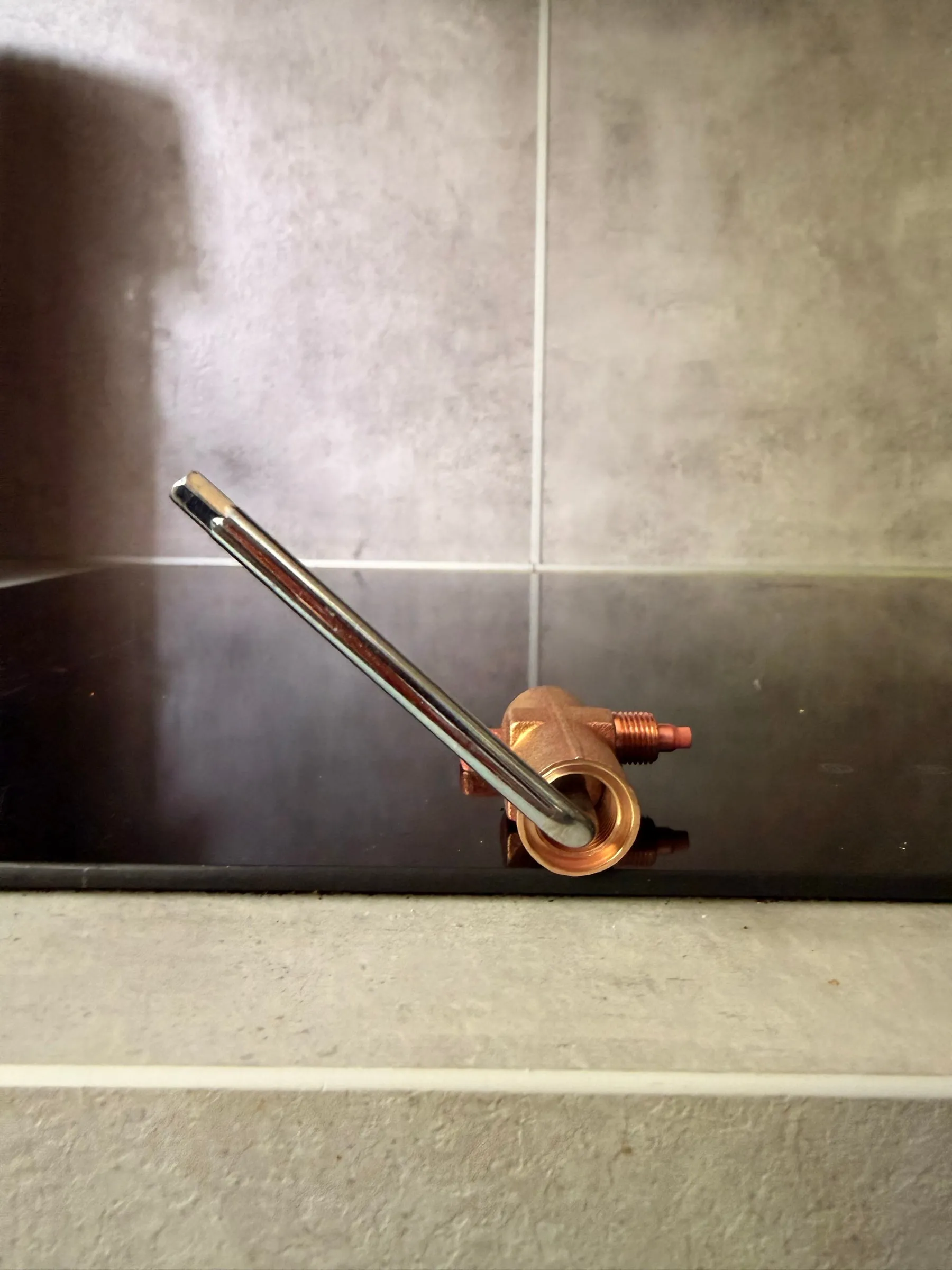 The brass over-pressure valve body on a dark hob with a long chrome 5 mm hex key inserted into the adjuster
