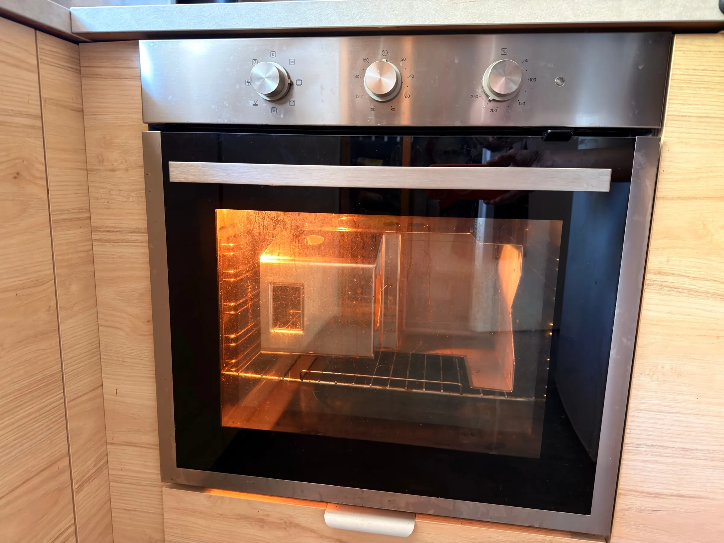 A built-in kitchen oven with the door closed, the polished espresso machine housing glowing orange inside behind the glass