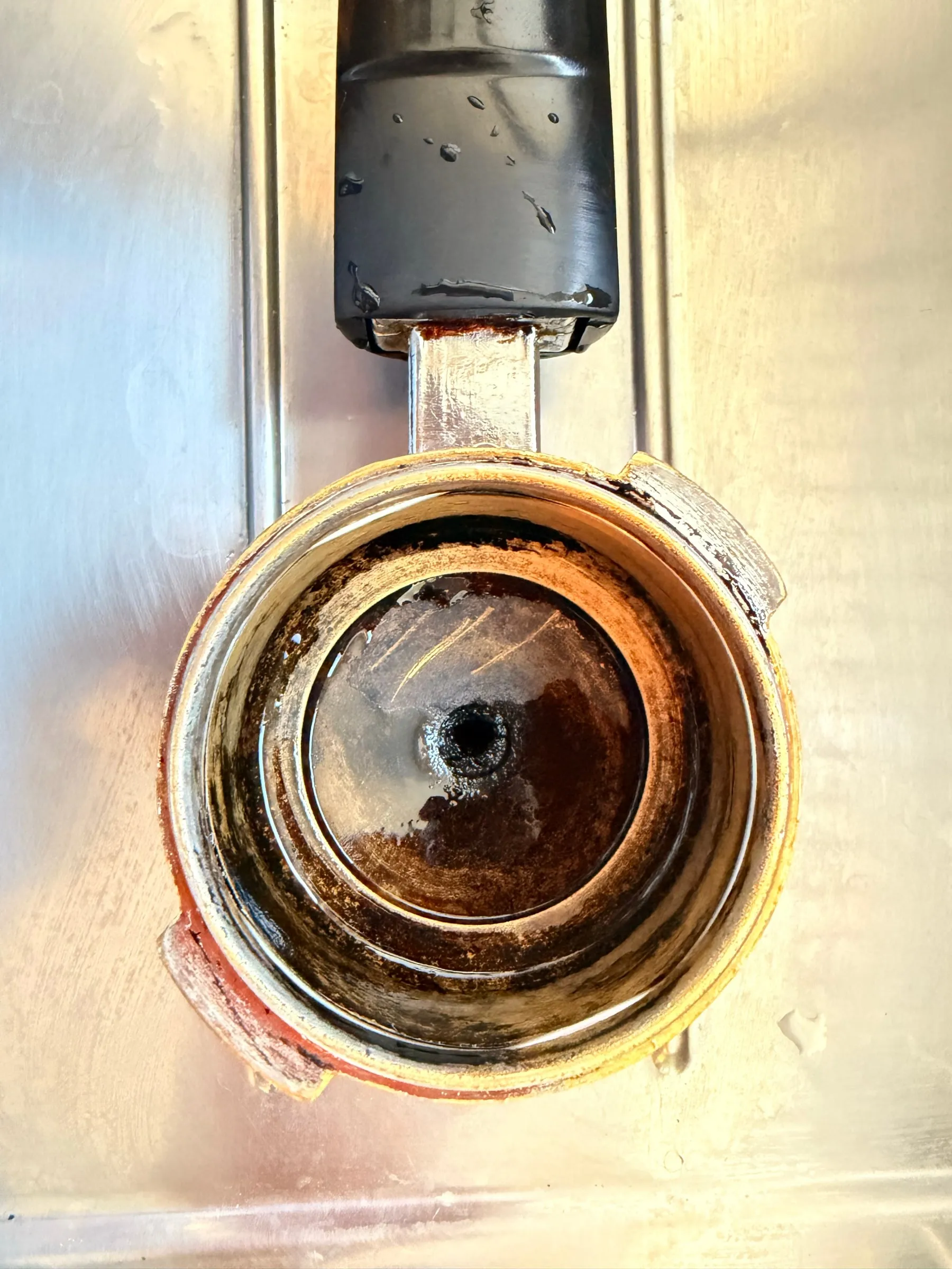 The portafilter lying in a sink in its cleaning bath, the basket dark brown with old coffee oils