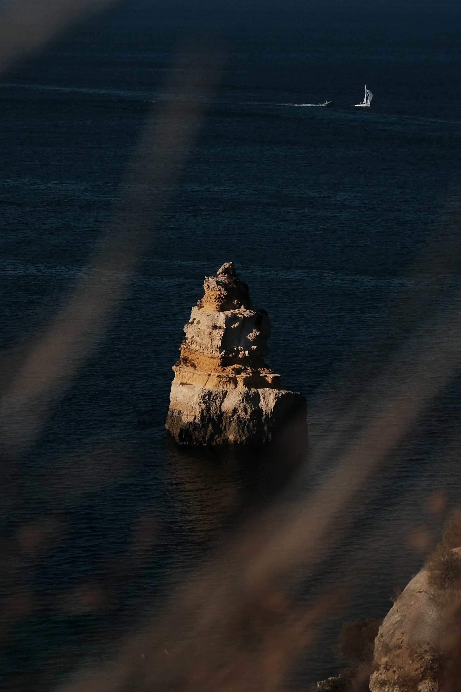 Single sea stack in deep blue water, a sailboat far out