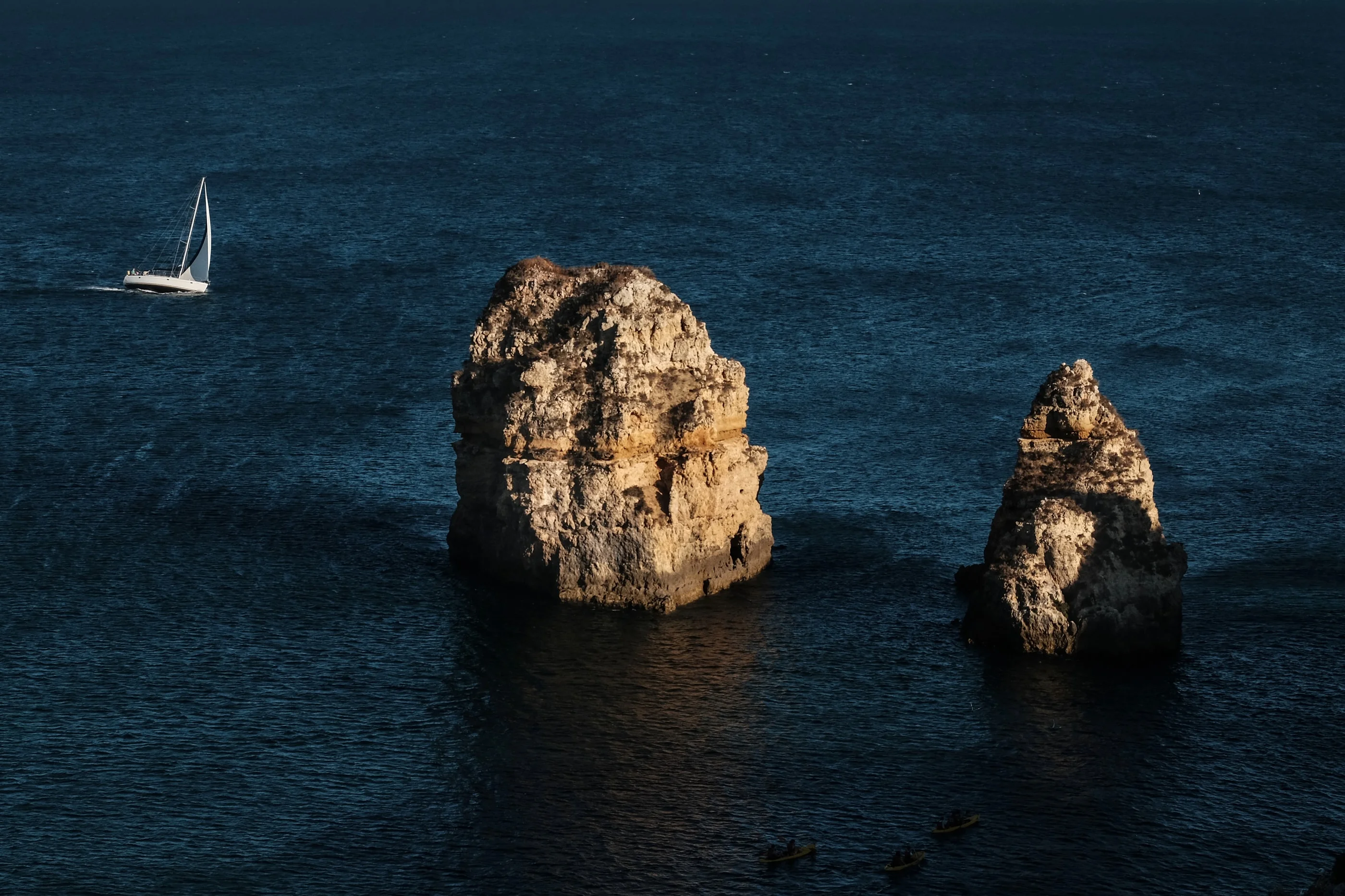 Two sandstone sea stacks in dark blue water with a sailboat beside them
