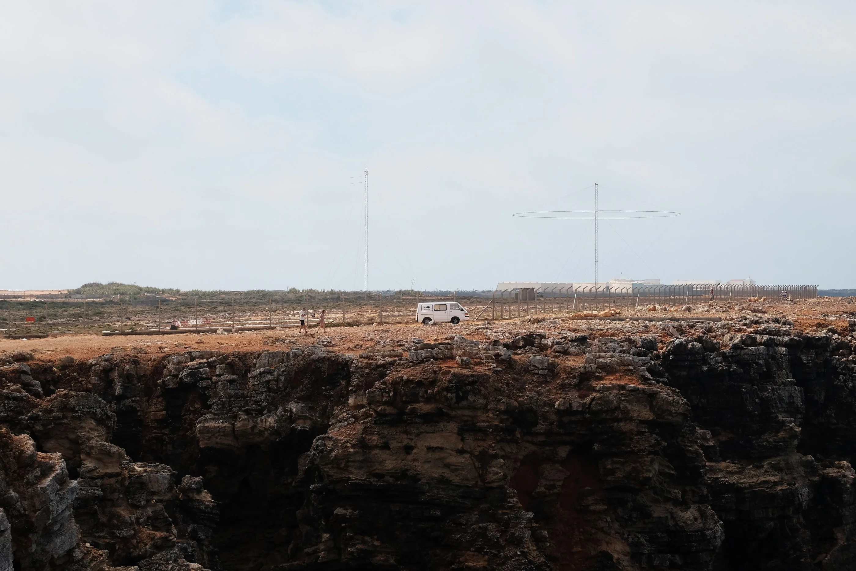 Flat clifftop under a hazy sky, a white van parked near the edge