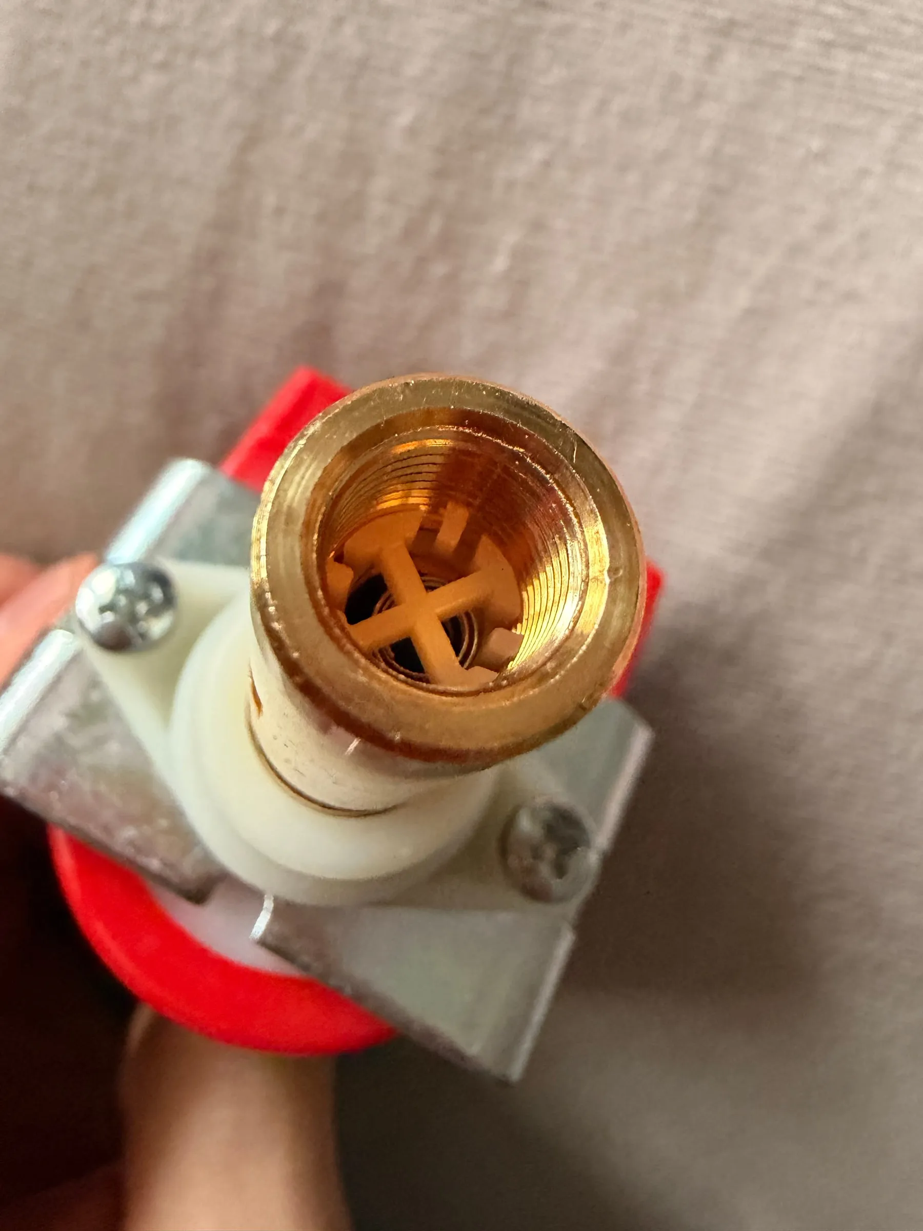 Looking straight down the brass outlet bore of the new pump: the internal thread and the orange plastic cross-shaped cage of the check valve