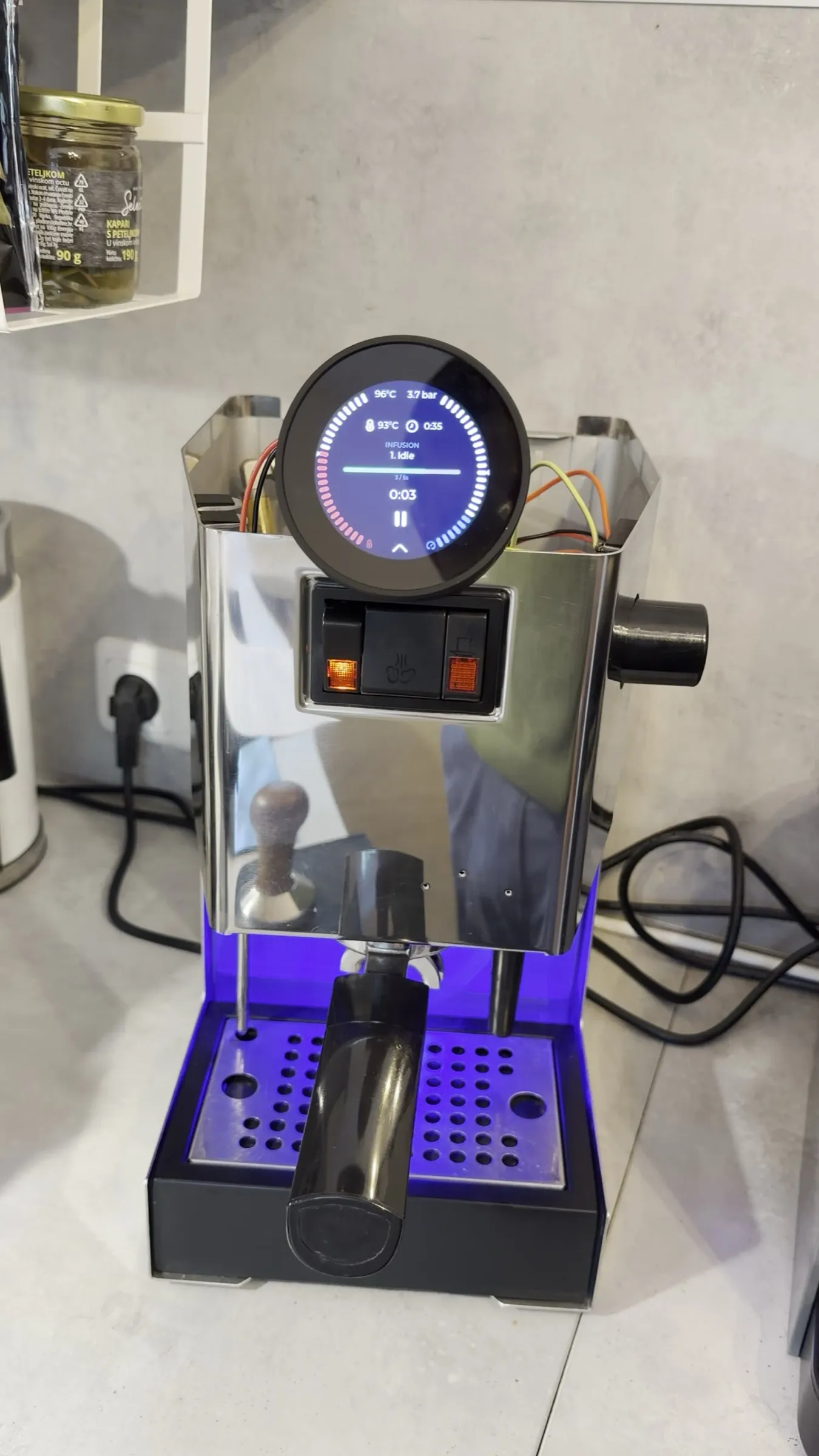The round display in the idle phase of the self-test, reading 96 degrees and 3.7 bar with the pump off, the blind filter locked into the machine on the kitchen worktop