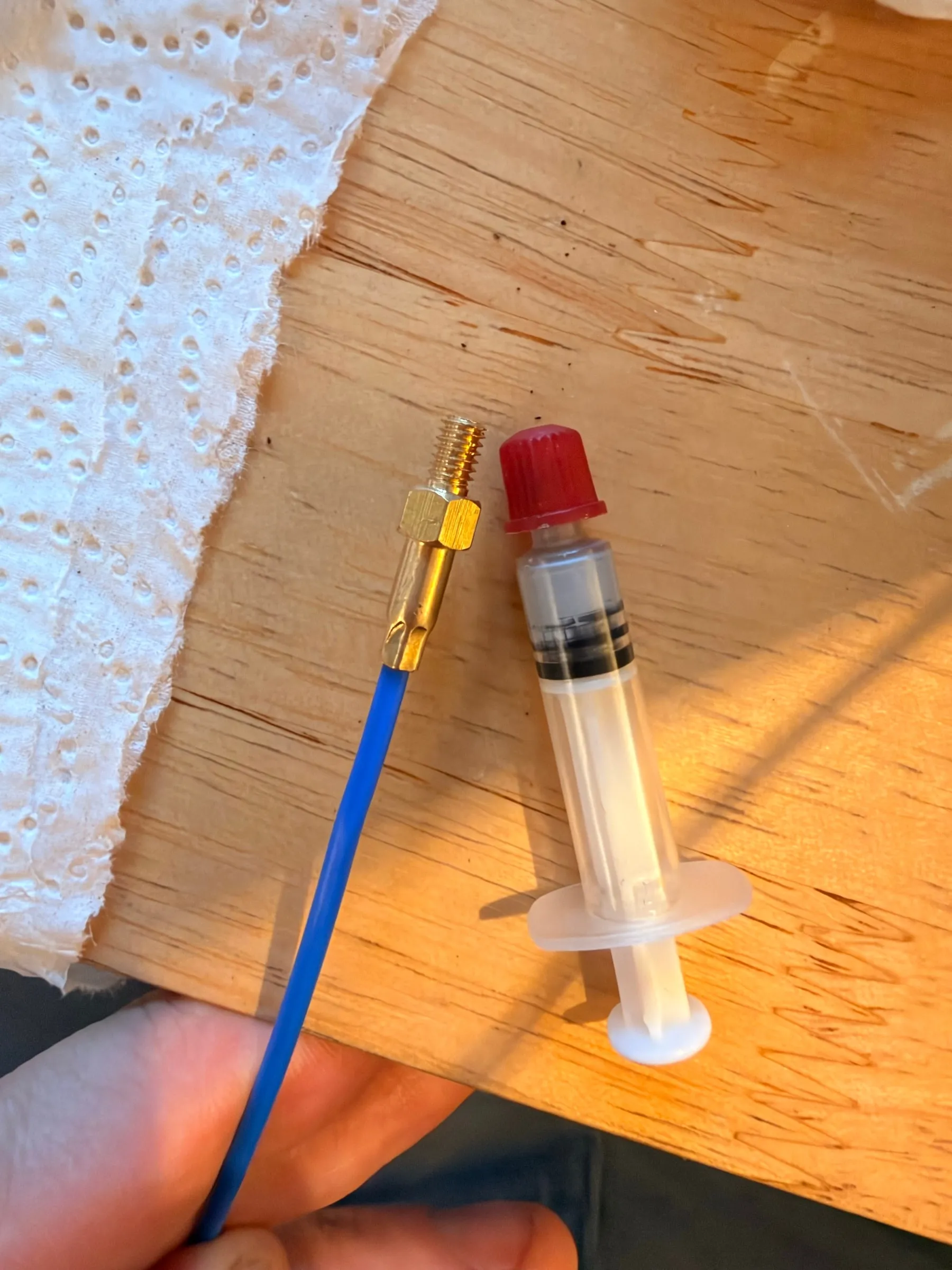 The M4 temperature probe on its blue cable and a small syringe of thermal paste with a red cap lying on a wooden table