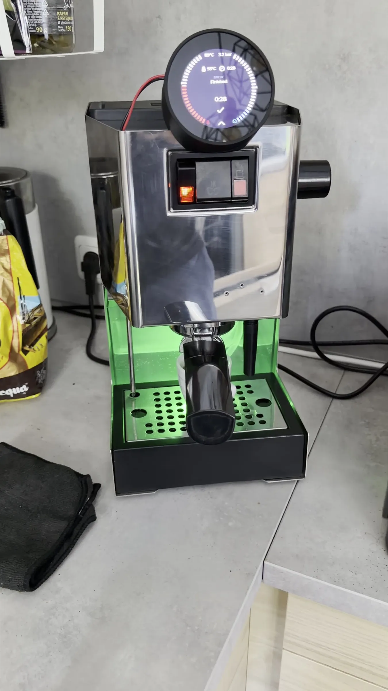 The machine on the kitchen worktop after the shot, the display reading Finished, the drip tray lit green, the portafilter locked in and a small cup beneath it