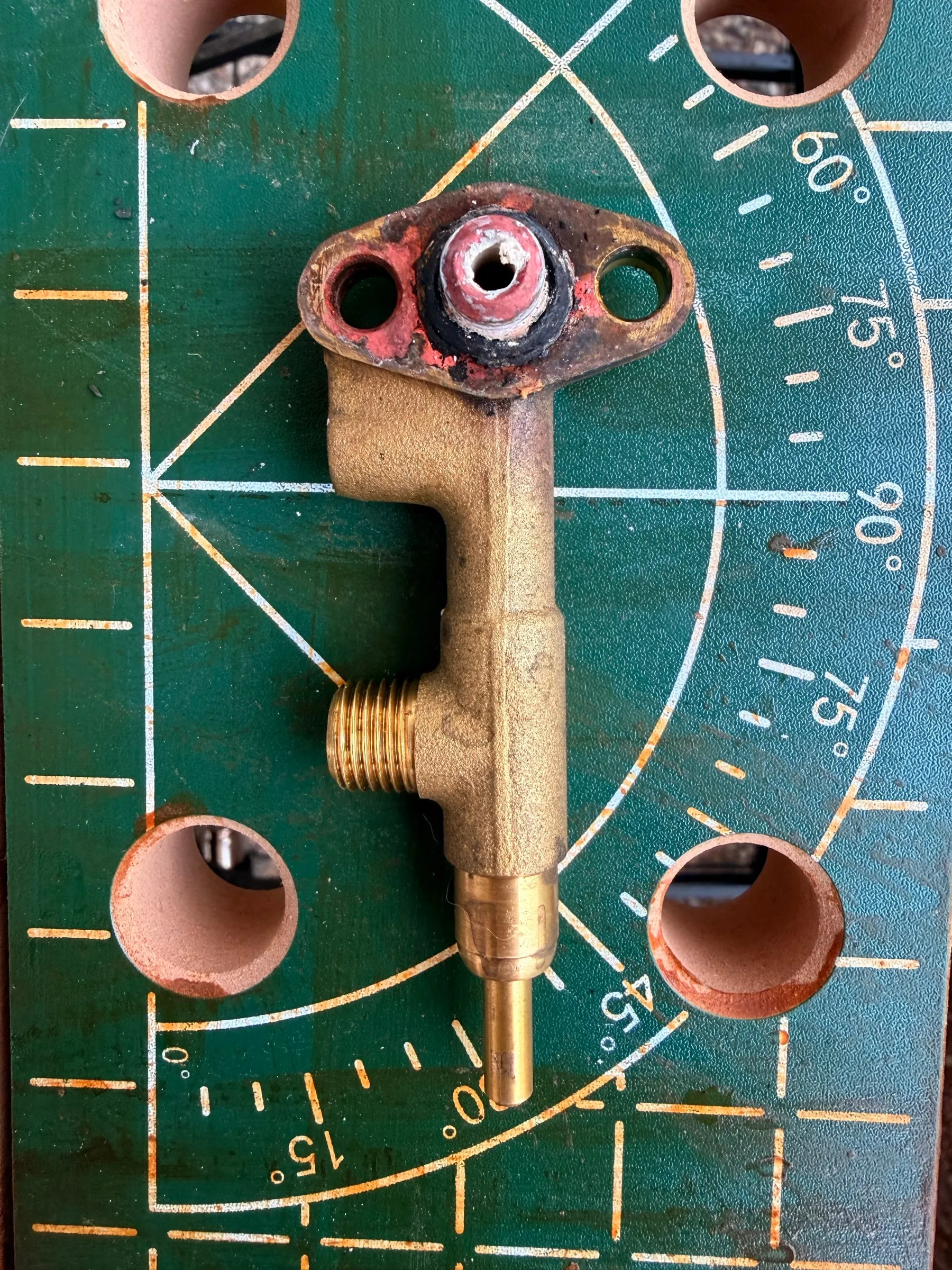 The brass steam valve on a green cutting mat right after it came off the boiler: the flange still carrying the red remains of its gasket, the body dull and crusted, the spindle for the knob pointing down