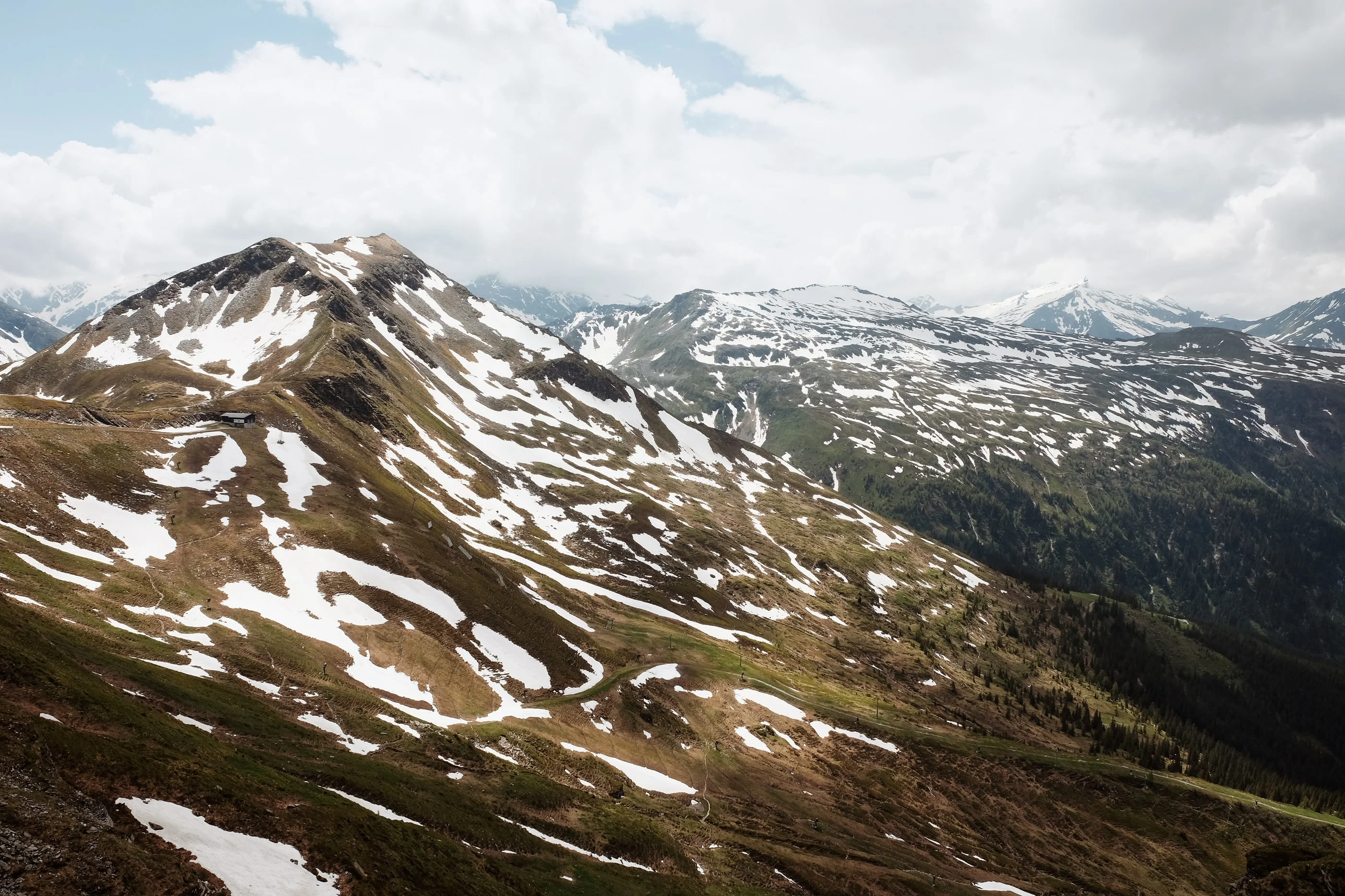 Grassy mountain ridge with patches of snow, more peaks behind