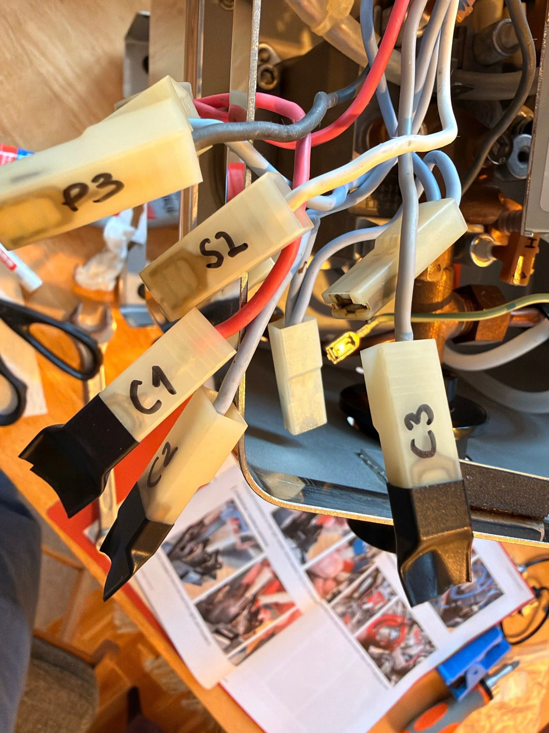 A bundle of grey and red wires with ivory spade connectors, each with a tape flag reading C3, C1, S2 and P3, the printed installation guide with its photos lying behind them