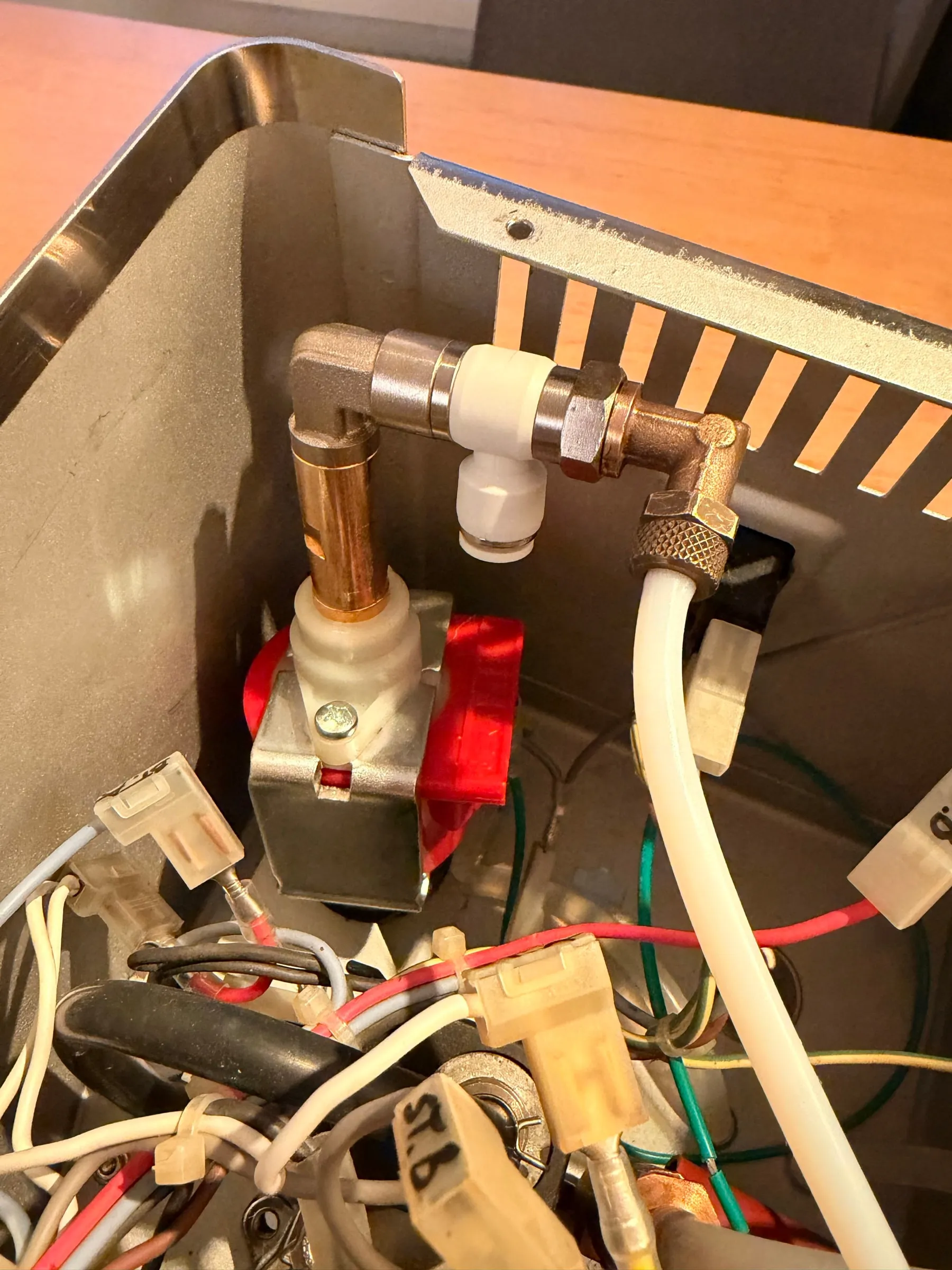 The new plumbing in the housing: the red pump below, the brass elbow on its outlet, the white T-piece on the elbow, the original brass fitting on the end of the T-piece with the hose to the boiler, and the sensor's hose leading off to the side