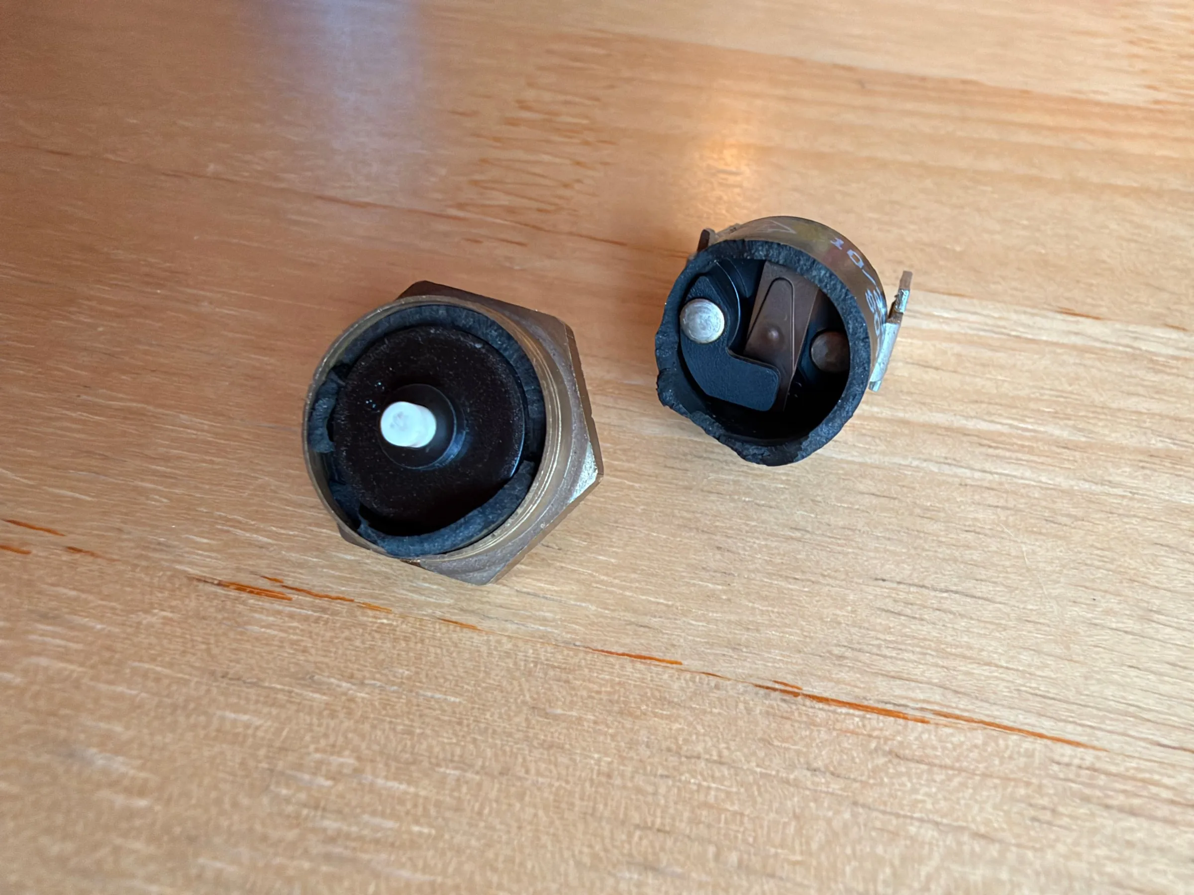 The two halves of the thermostat on the wooden table, seen from above: the brass base with the ceramic pin, and the plastic cap with its contacts