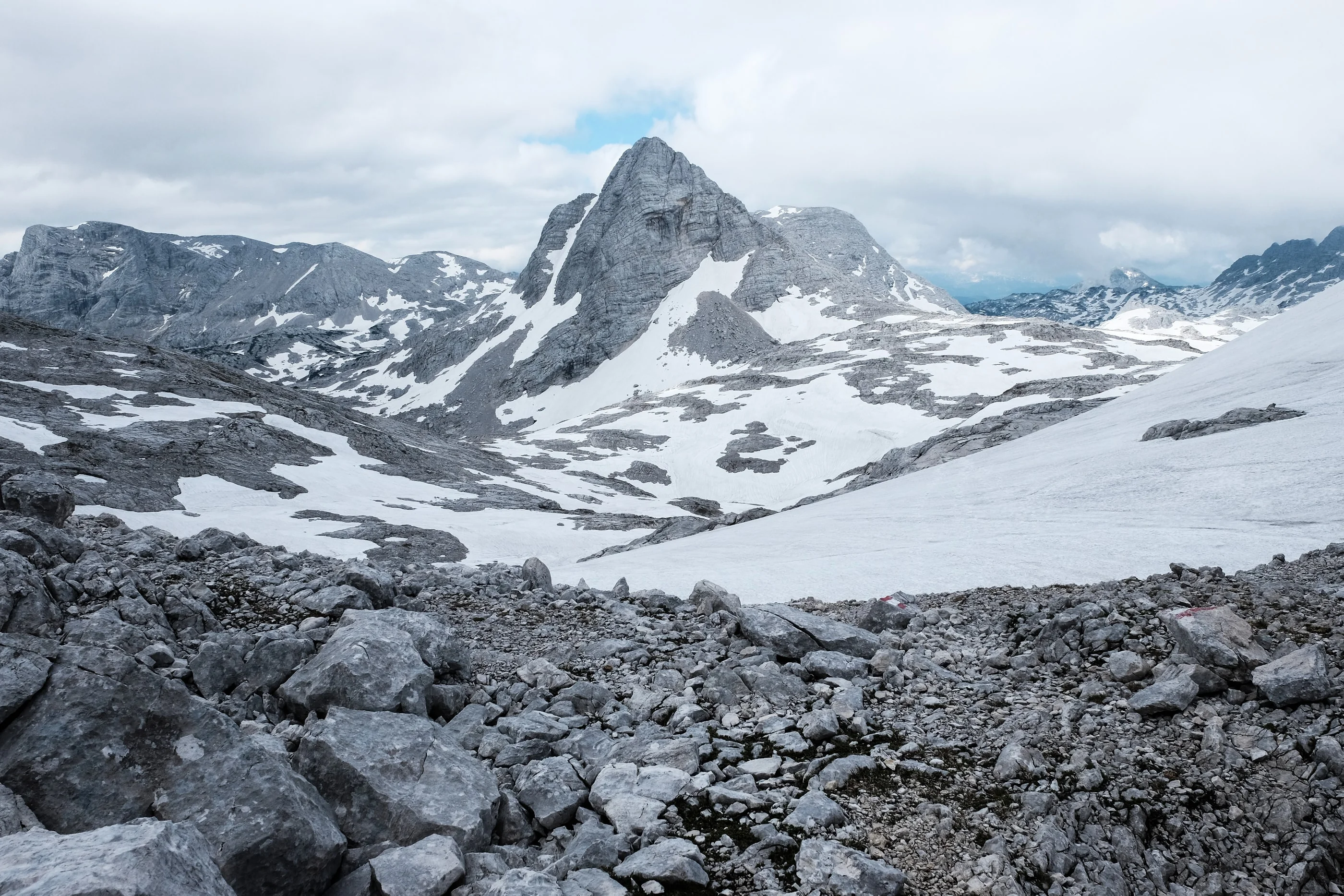 Boulder field and snowfields below a pointed limestone peak