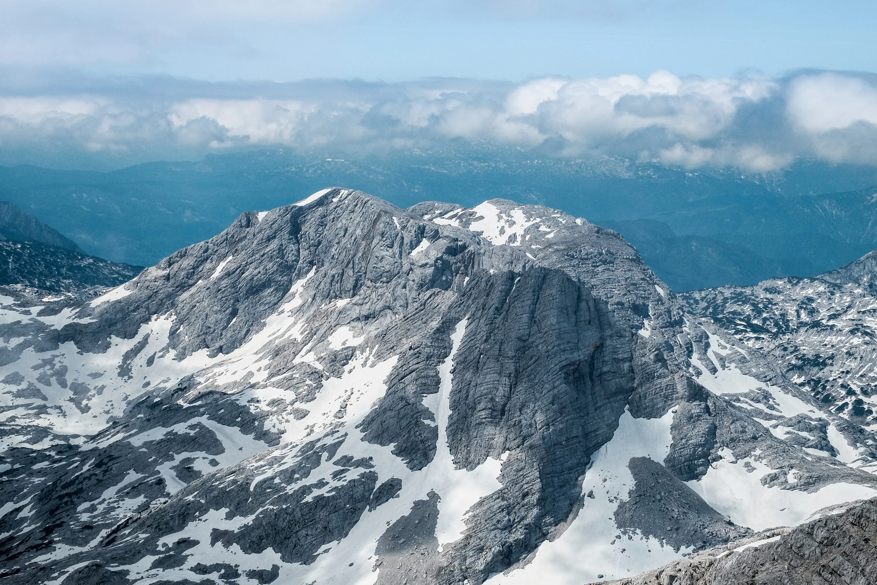 View from the summit over snowy limestone mountains under a band of clouds