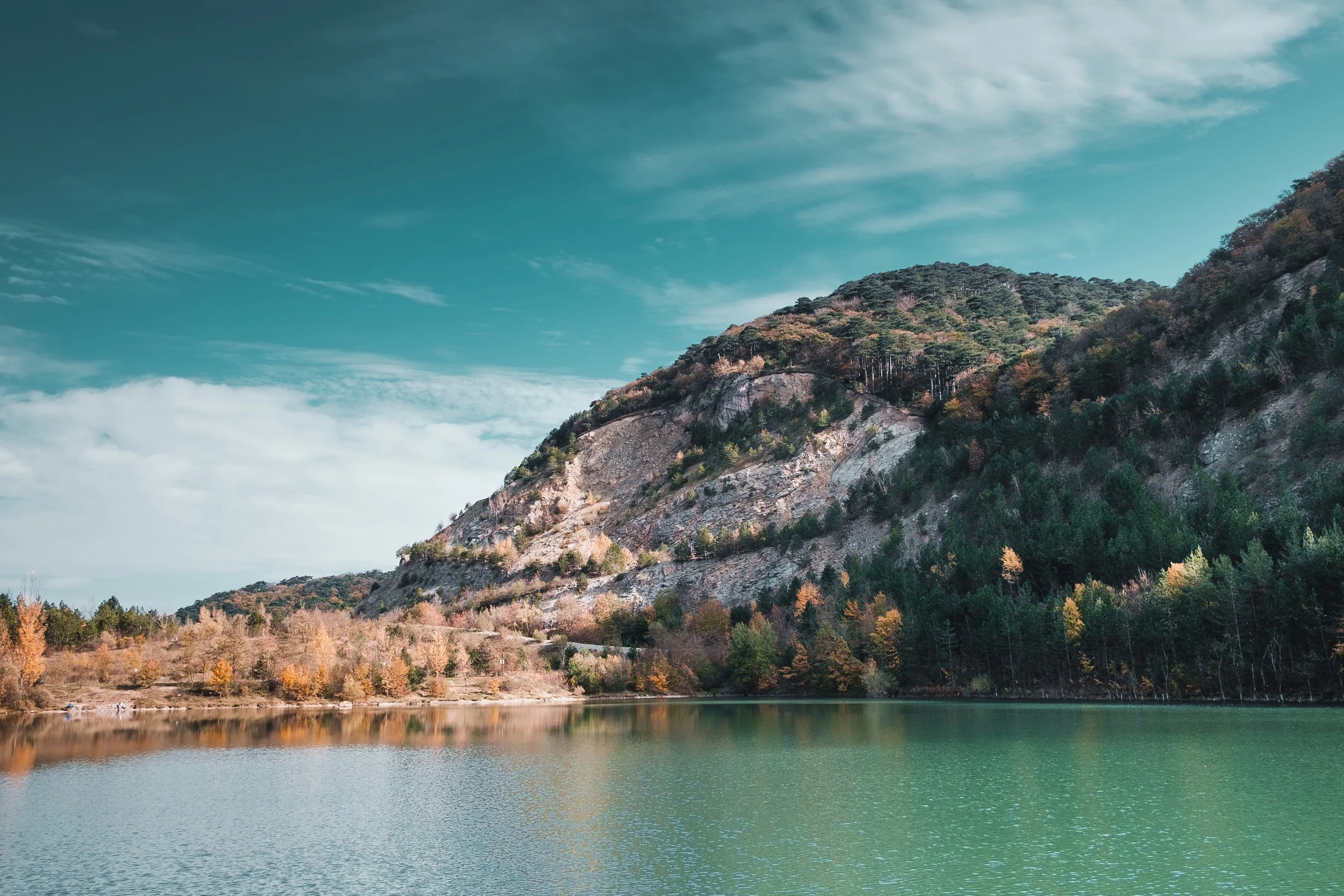 Lake below a rocky hill with autumn trees