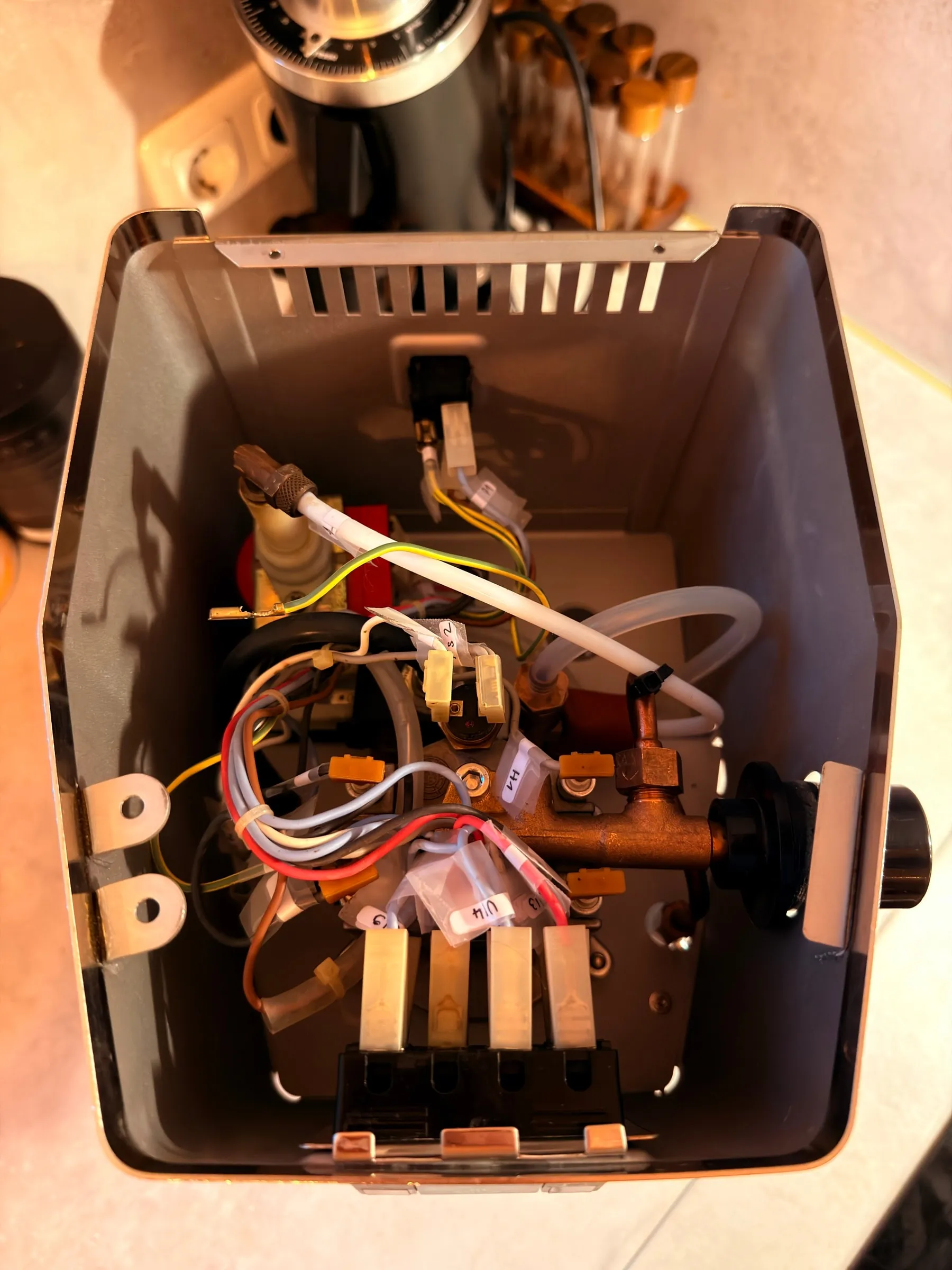 Top-down view into the fully rewired housing: the brass steam valve, the boiler with all labelled cables connected, the four-way switch block at the bottom, the grinder blurred in the background