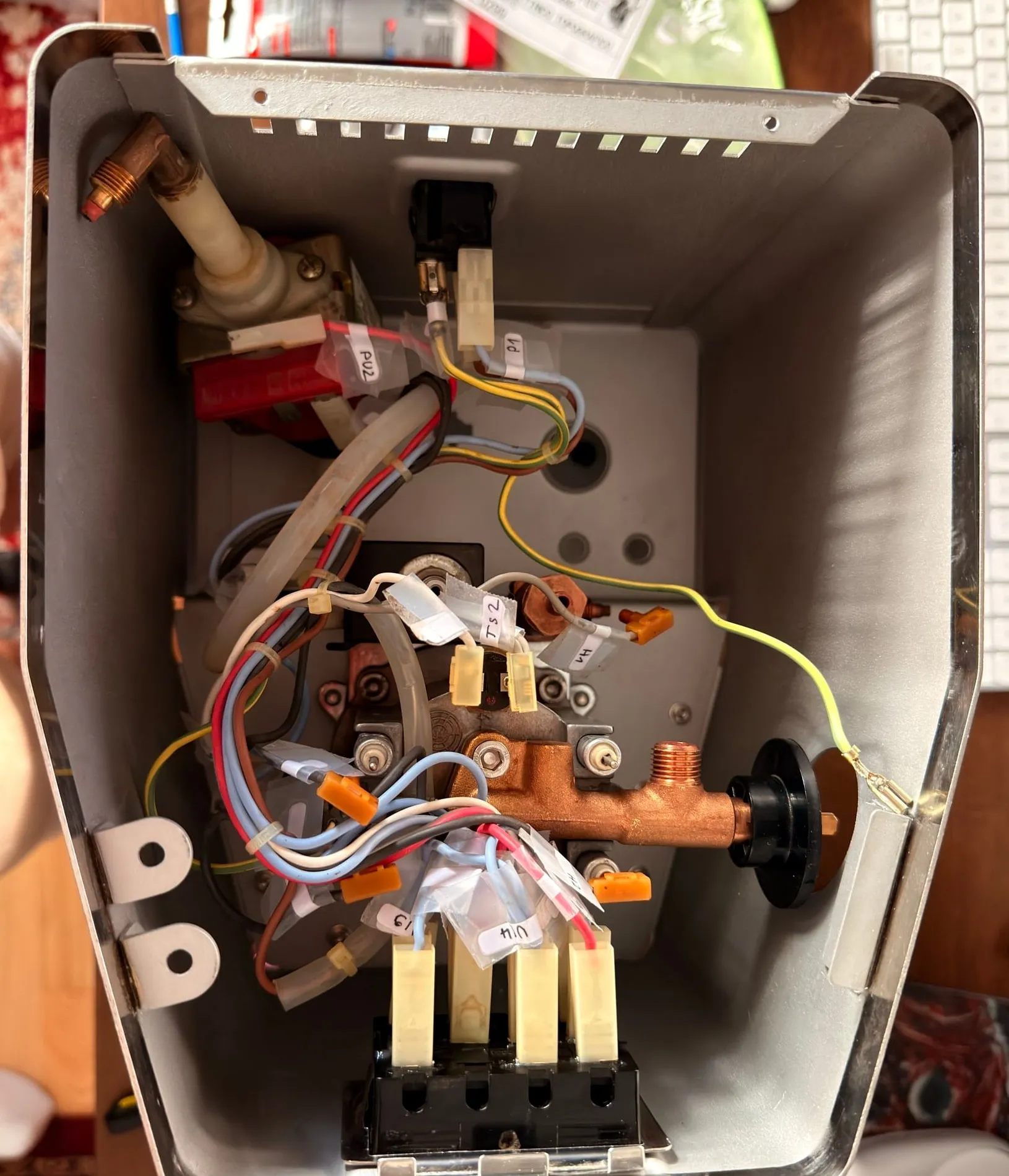 Looking down into the housing during reassembly: boiler, brass steam valve with its black knob and the red Ulka pump back in place, the loom being reconnected with tape labels reading PU2, P1, TS2 and U1/4, the yellow-green earth wire routed to the frame